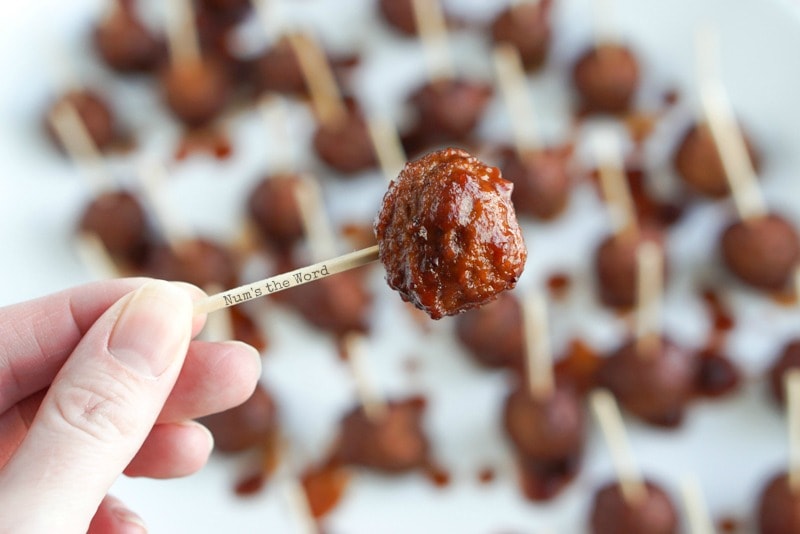 Cranberry Barbecue Meatballs - single meatball in sauce on toothpick with hand holding it.