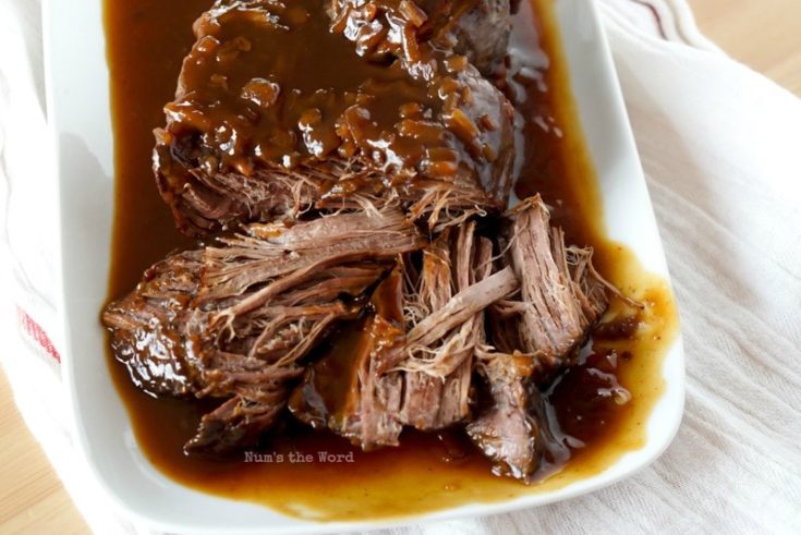 Cranberry Pot Roast - cooked roast on platter with sauce poured on top. Part of roast has been pulled to show tender insides.