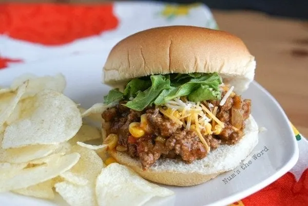 Mexican Sloppy Joes - topped with lettuce and cheese with a pile of potato chips next to sandwich