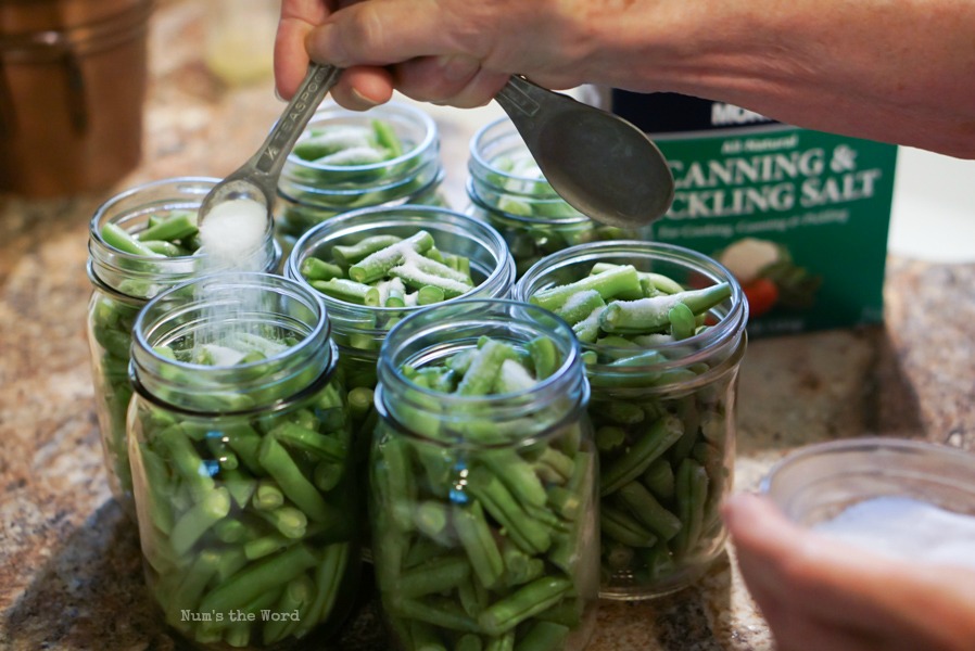 canning salt being added to jars of green beans