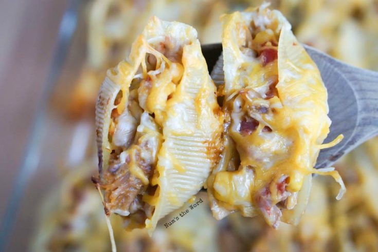 two stuffed shells, cooked and on a wooden spoon about to be placed on a plate.