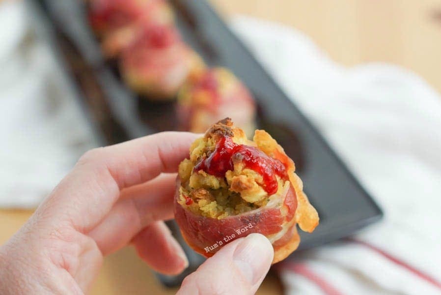 Bacon Wrapped Stuffing Bombs - hand holding a bacon bomb with a dollop of raspberry sauce.