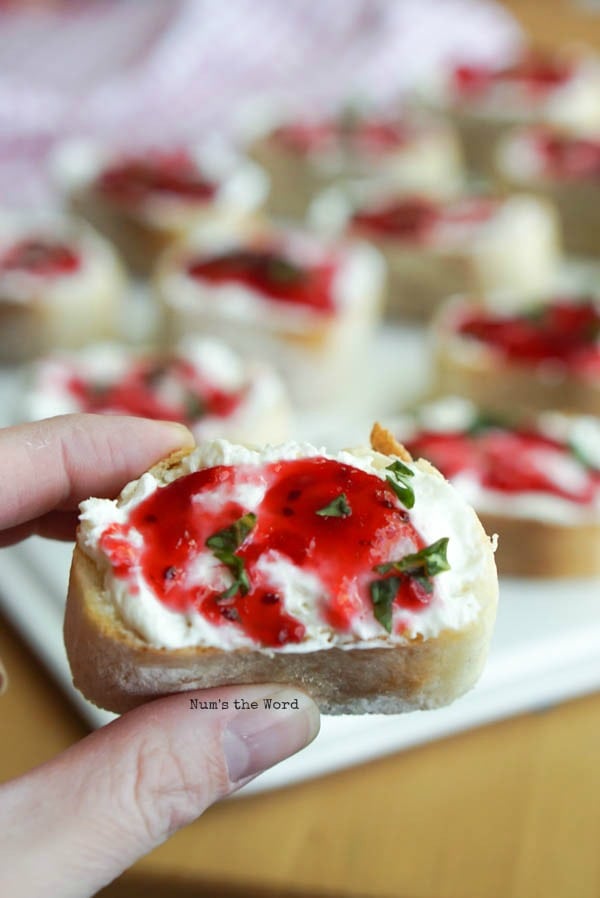 Leftover Cranberry Sauce Bruschetta - fingers holding up a single bruschetta close to camera lens