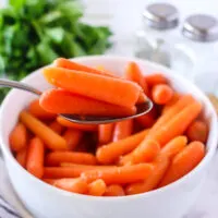 spoon scooping candied carrots out of serving bowl