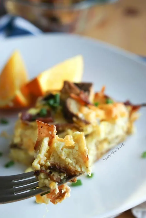 Bacon, Egg & Cheese Strata - fork full of strata with slice of strata in background.