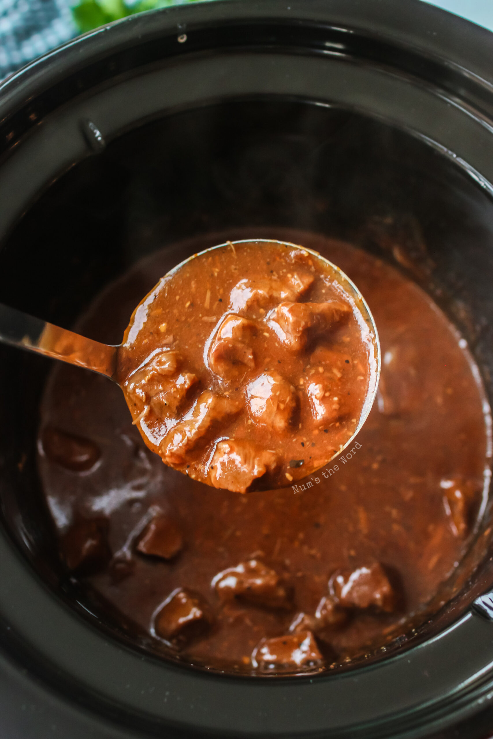 Ladle scooping out beef tips with gravy out of crock pot