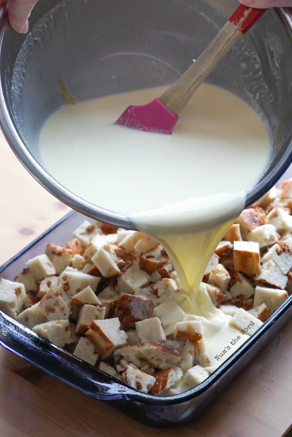Custard being poured over bite sized bagel pieces in casserole dish.