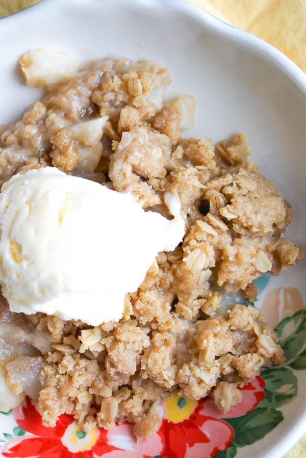 close up image of pear crisp in bowl with ice cream on top
