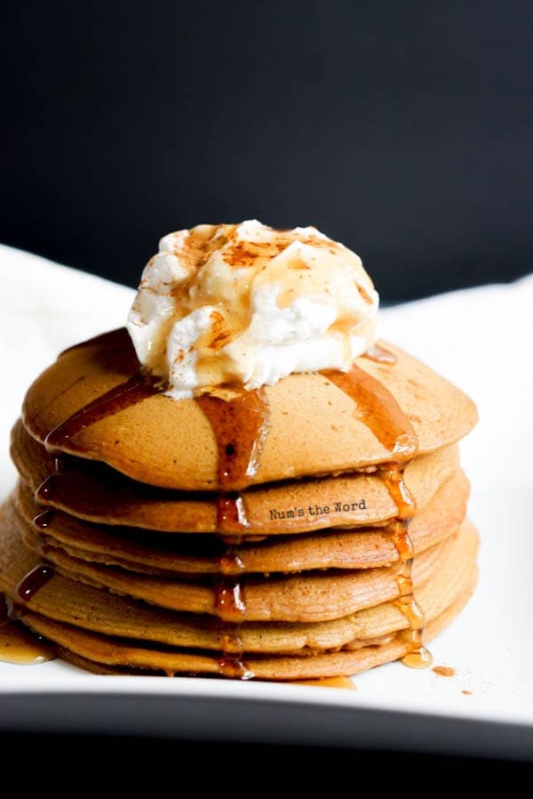 Gingerbread Pancake Recipe - pancake stack on plate with whipped cream and syrup drizzling down the top.