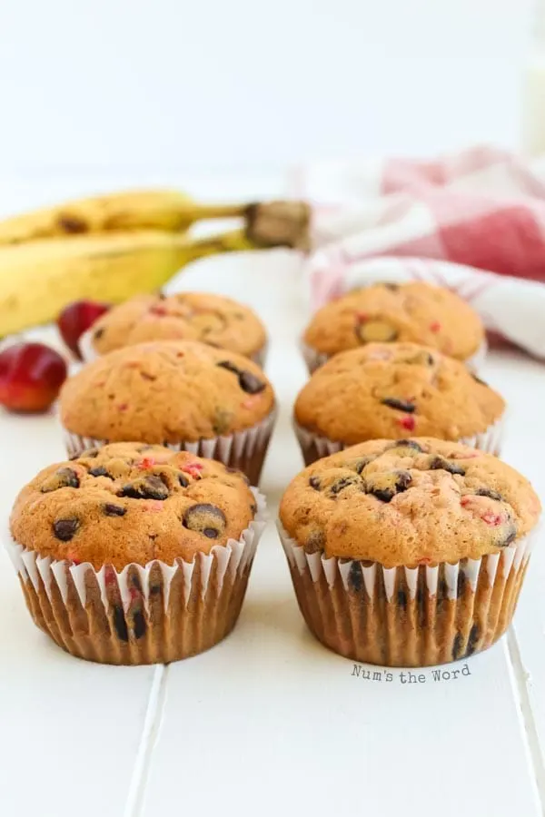 Banana Chocolate Chip Muffins - 6 muffins on counter with bananas and cherries in background