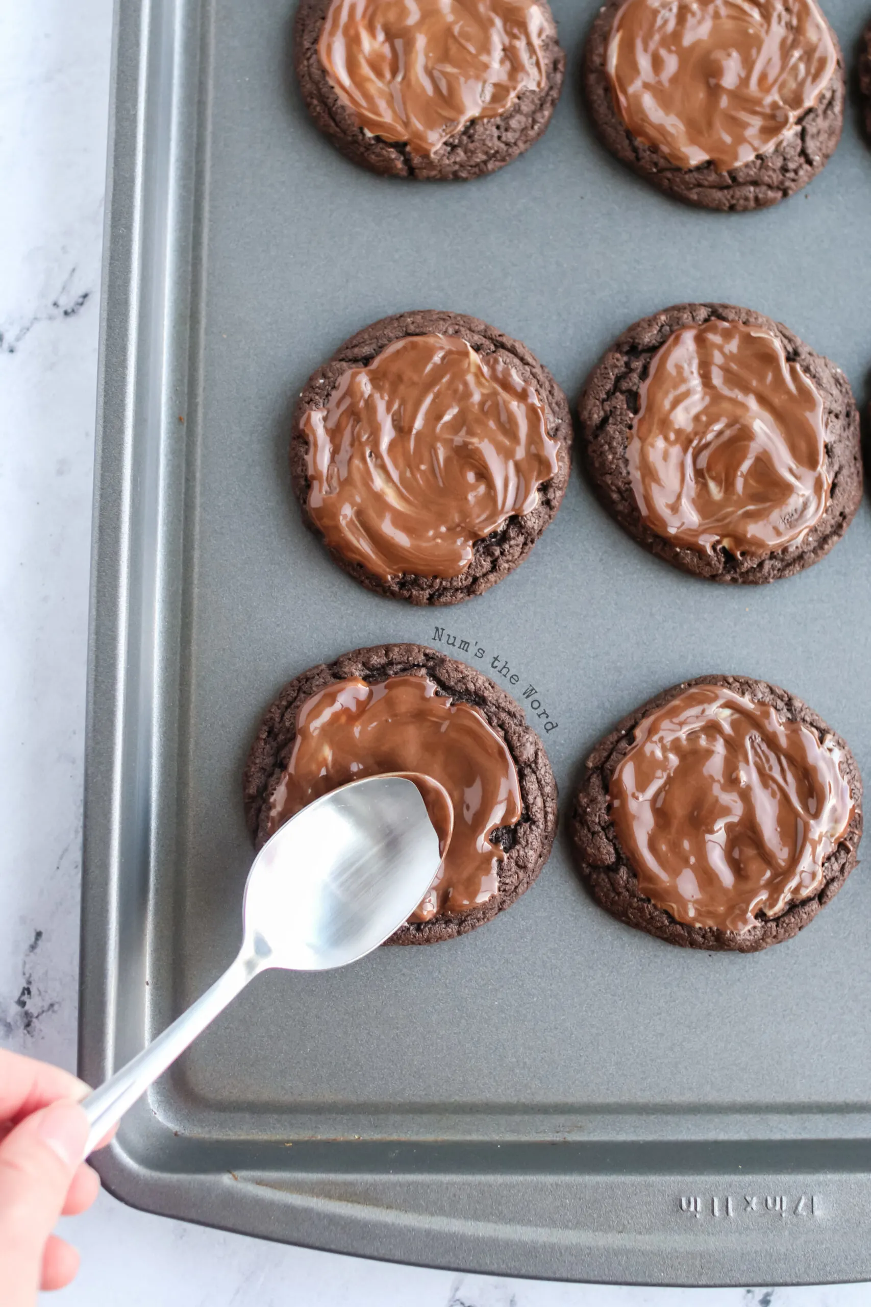 Chocolate has melted and a spoon is spreading it around on top of cookie