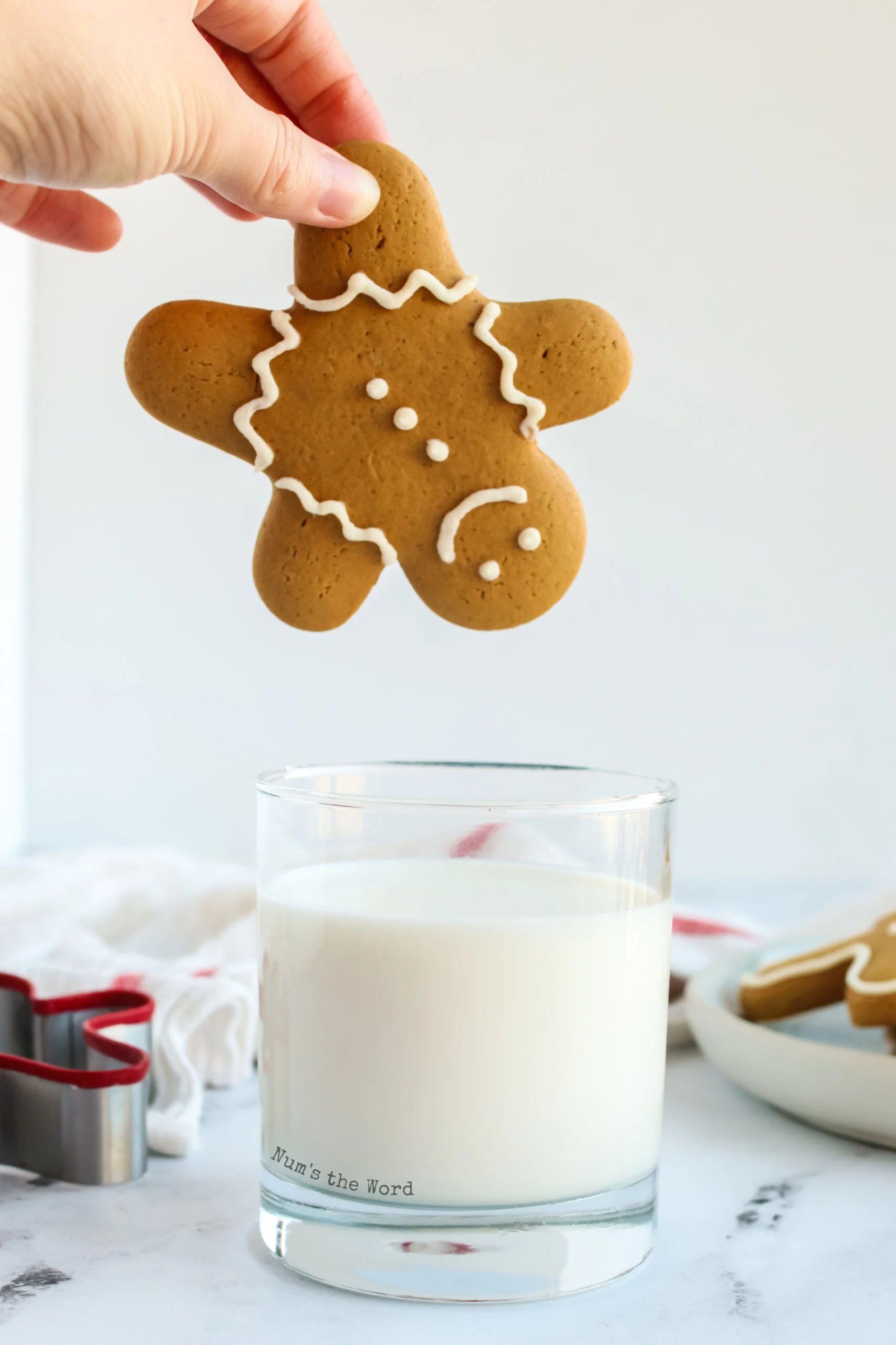 decorated gingerbread cookie being held upside down and ready to be dunked into a glass of milk