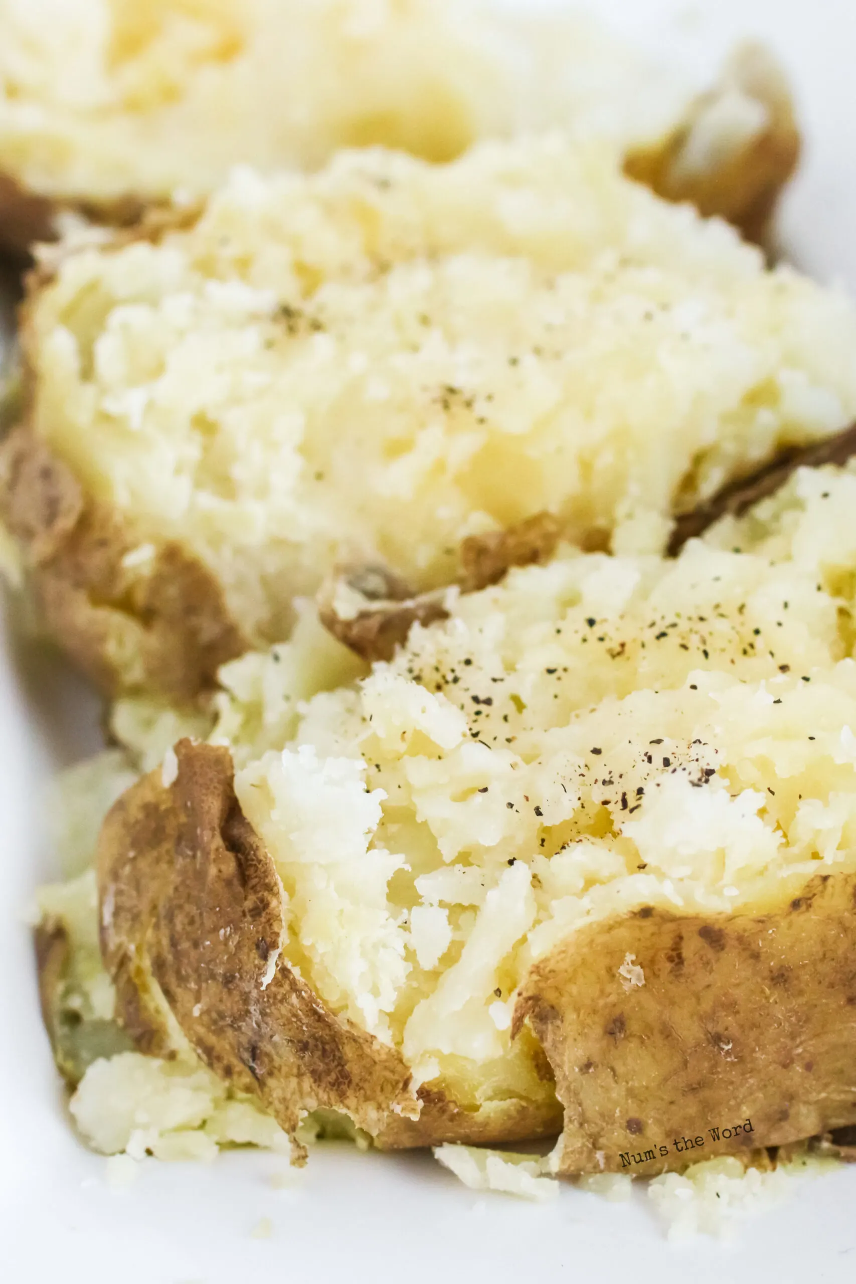 close up of two baked potatoes on platter. Closest one has salt and pepper on it.