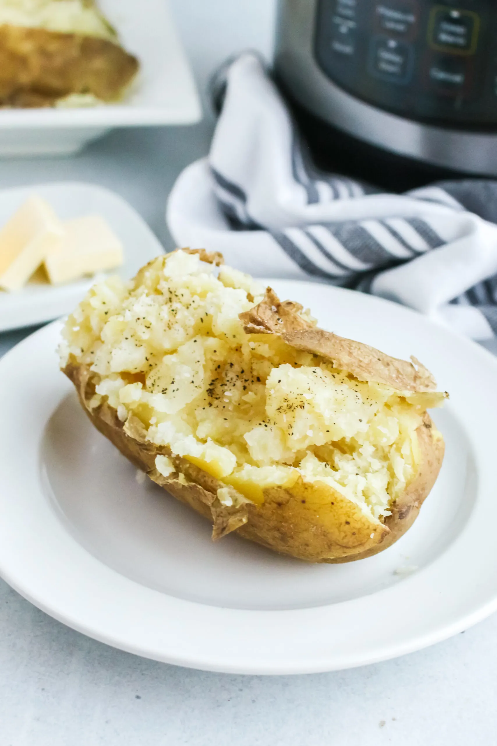 a single baked potato on a plate with instant pot in background