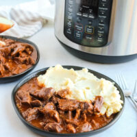 Instant pot in background with two plates of mashed potatoes and beef paprikash on a plate next to it.