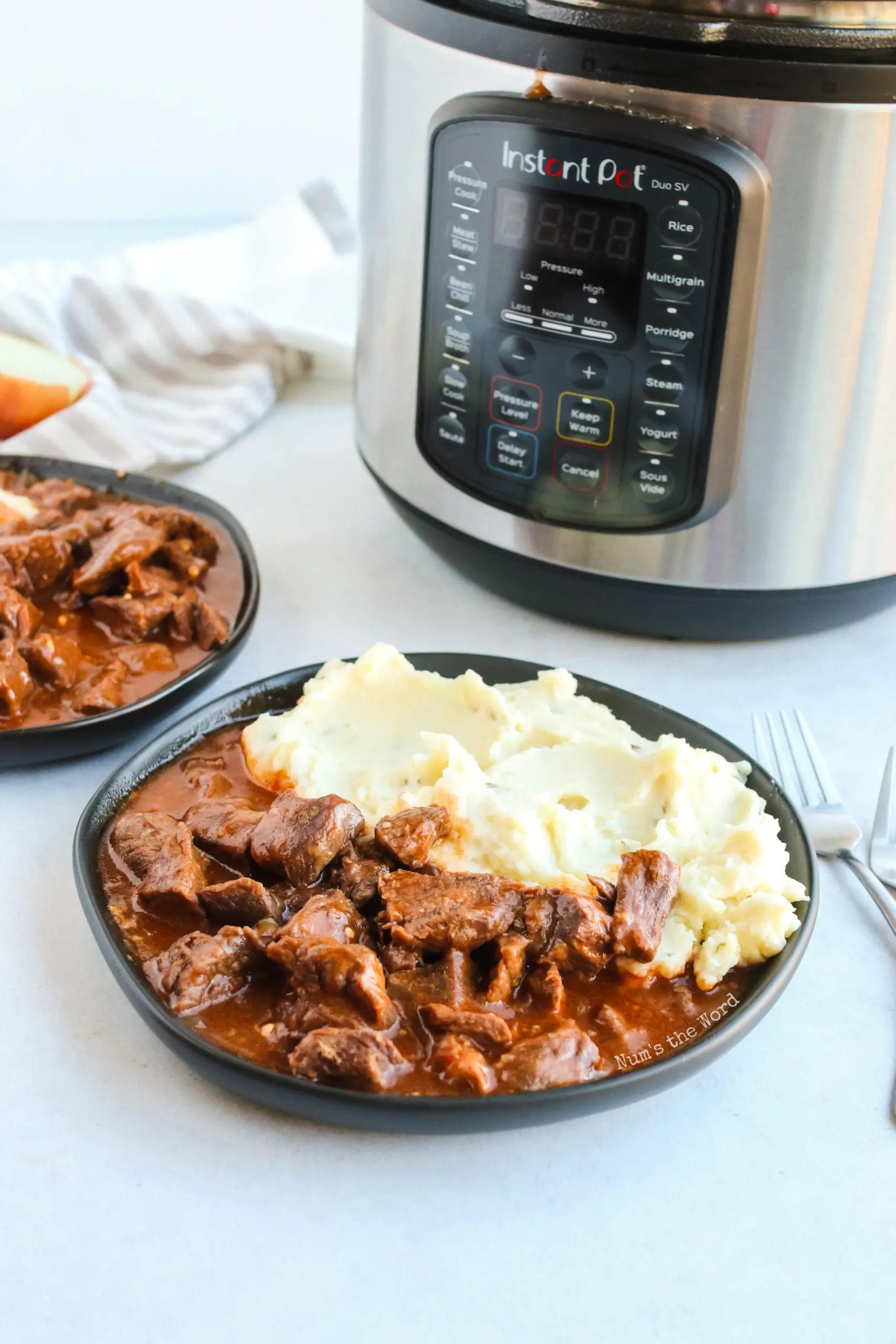 Instant pot in background with two plates of mashed potatoes and beef paprikash on a plate next to it.