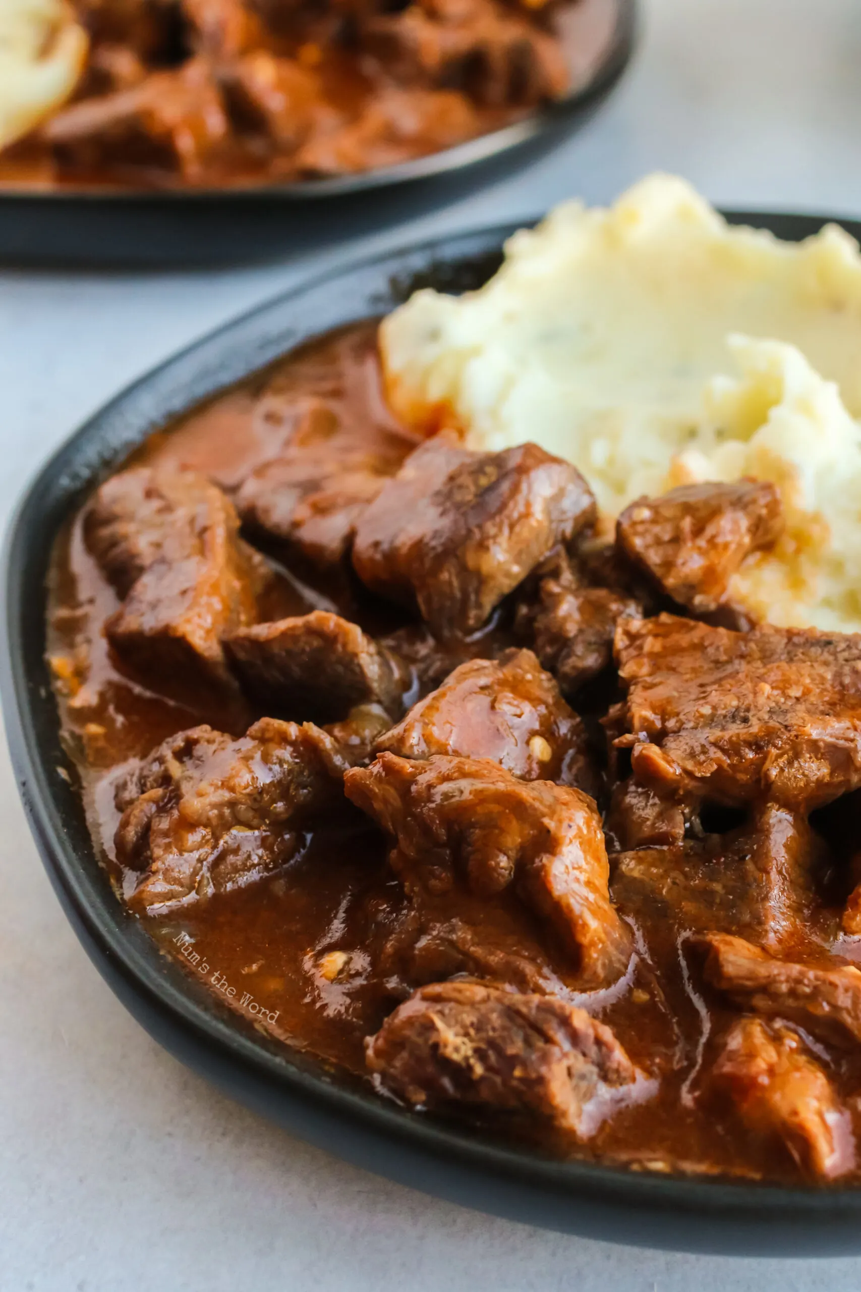 close up of beef paprikash on a plate with mashed potatoes.