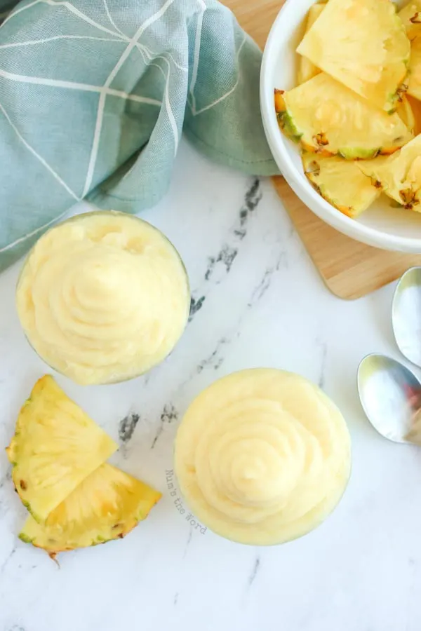 zoomed out image of two cups dole whip with bowl of fresh pineapple.