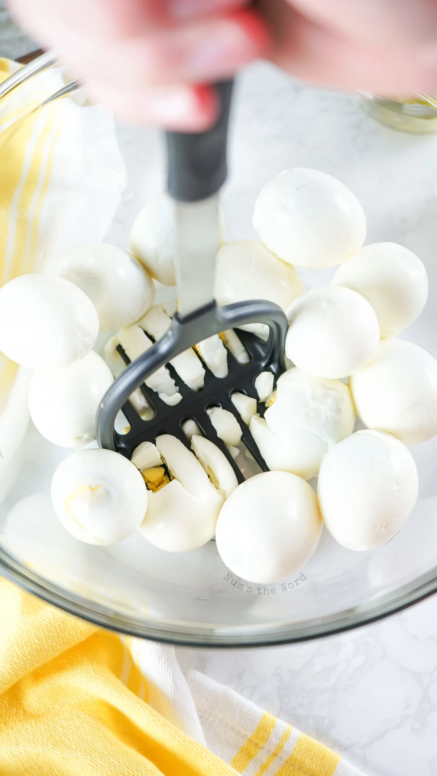 Potato masher being used to dice hard boiled eggs.