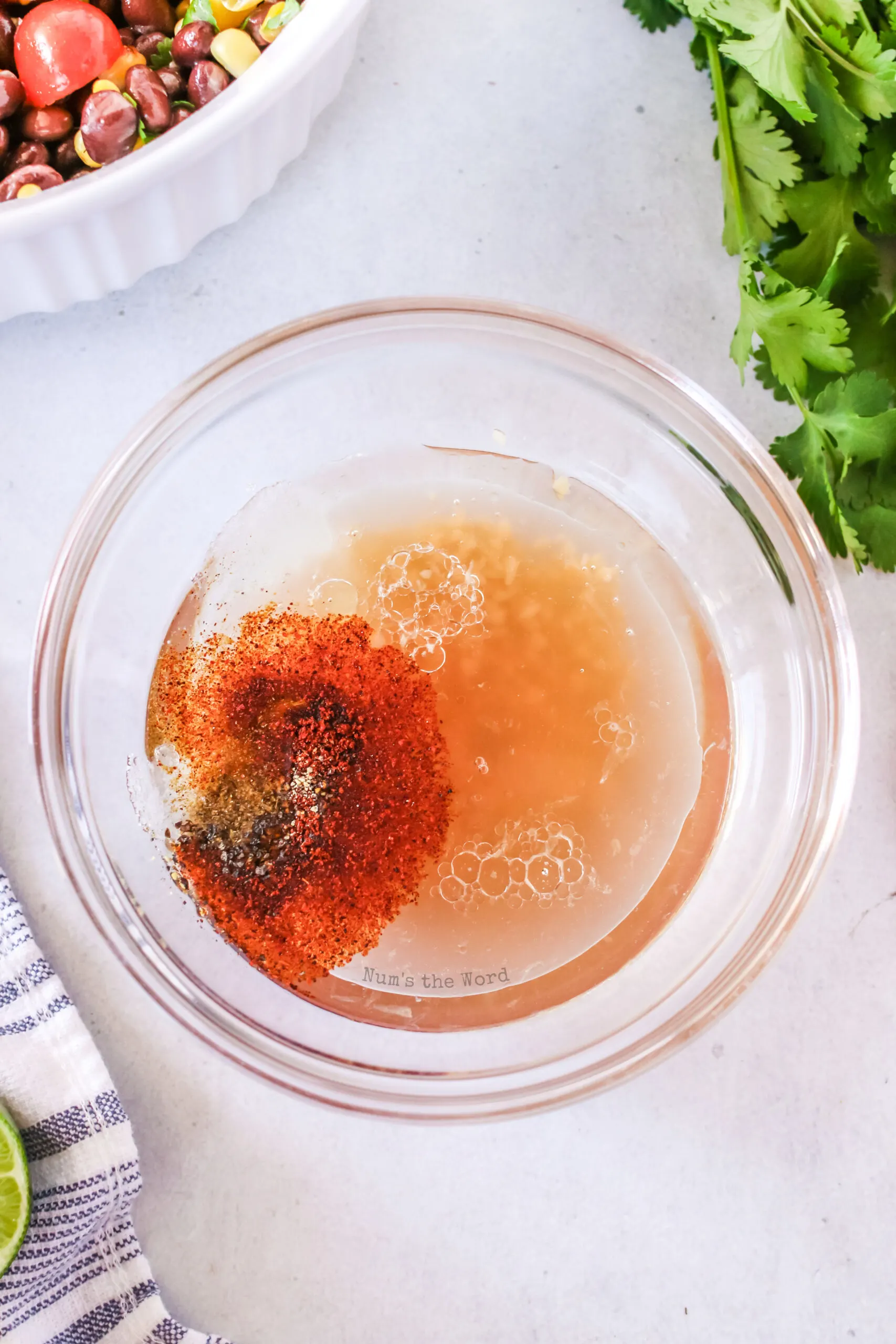 olive oil, red wine vinegar, lime juice, garlic, white sugar, cumin, chili powder, salt and black pepper all added to a bowl.