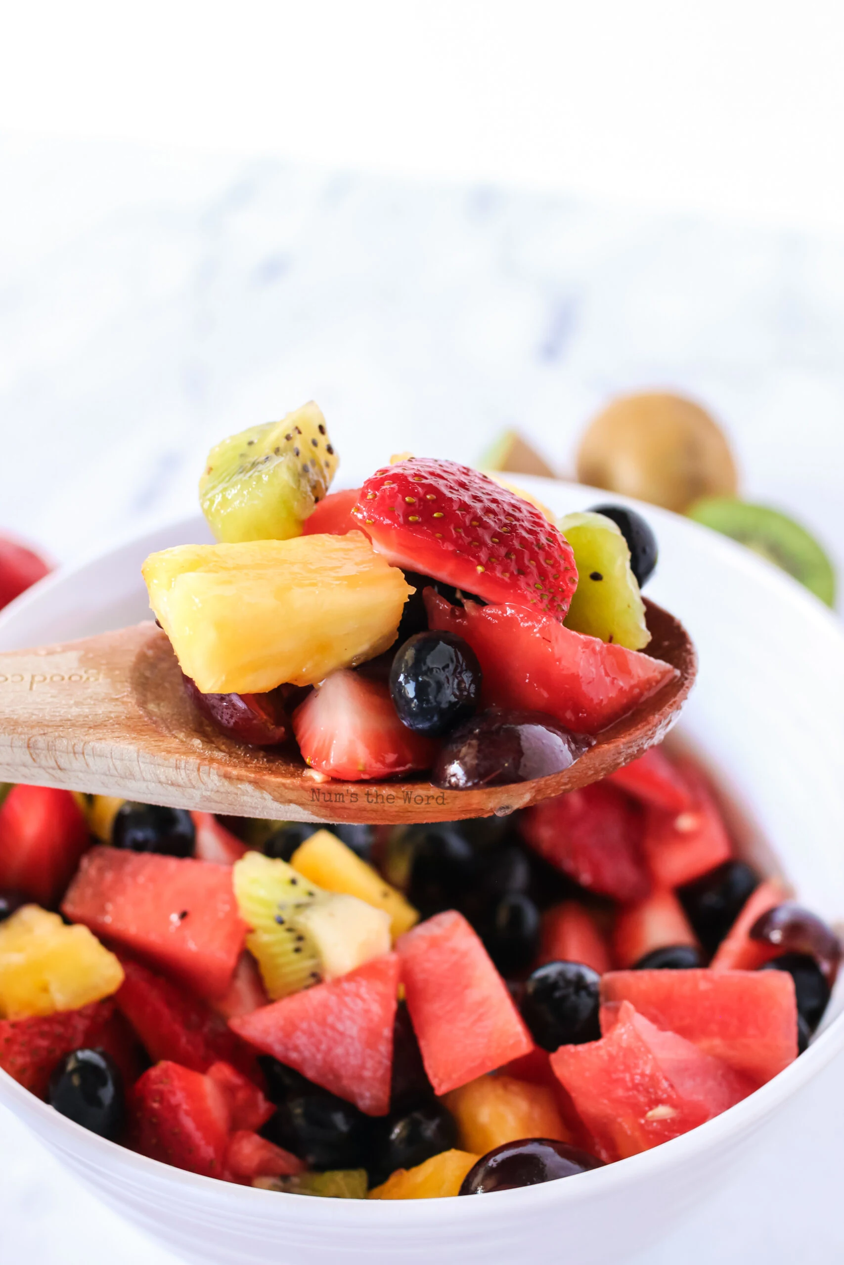 side view of fruit salad in bowl with a wooden spoon holding some above the bowl.