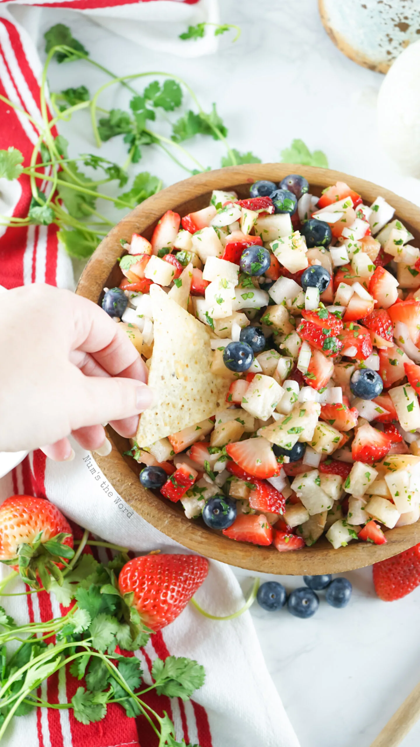 bowl of fruit salsa with a hand scooping out salsa onto a tortilla chip