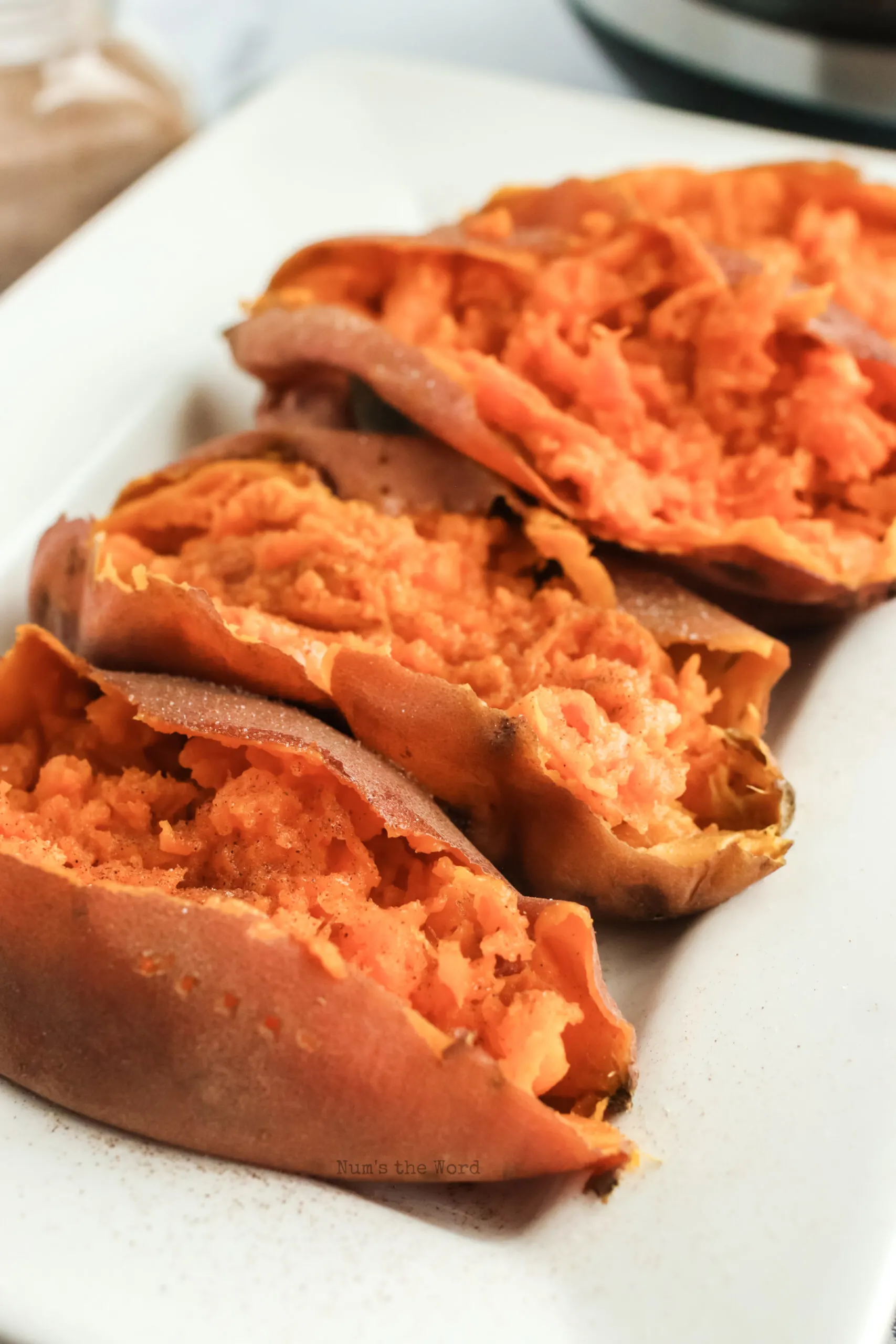 side view of 4 sweet potatoes on a platter, sliced open and ready to serve.