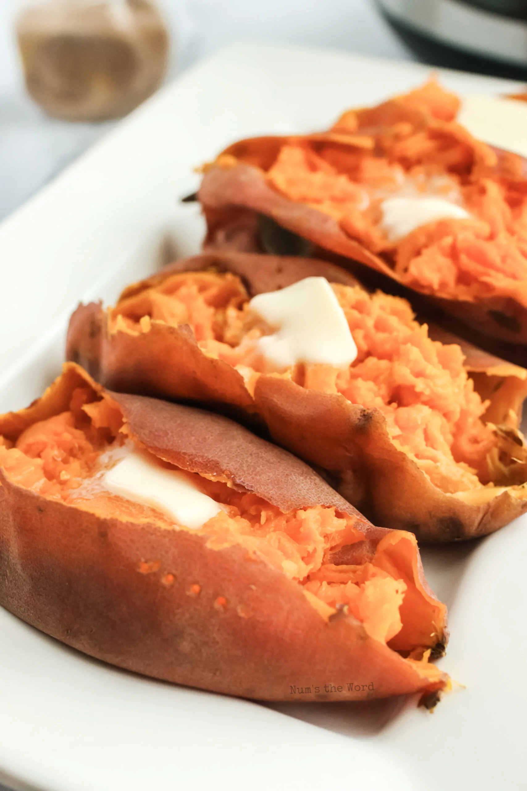 3 sweet potatoes with butter dolloped on top, side view angle