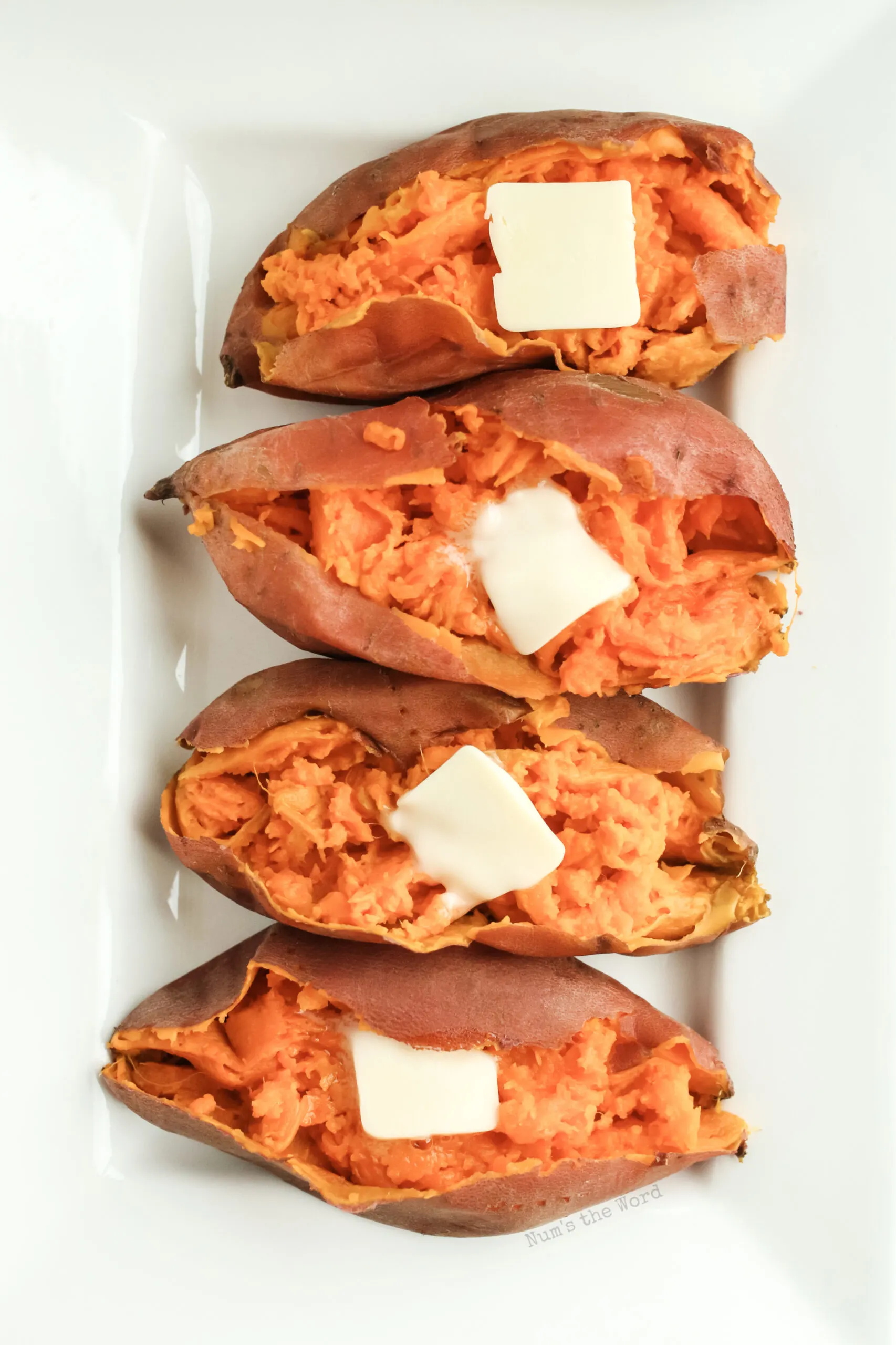 4 sweet potatoes on platter with dollops of butter. Image taken from the top down.