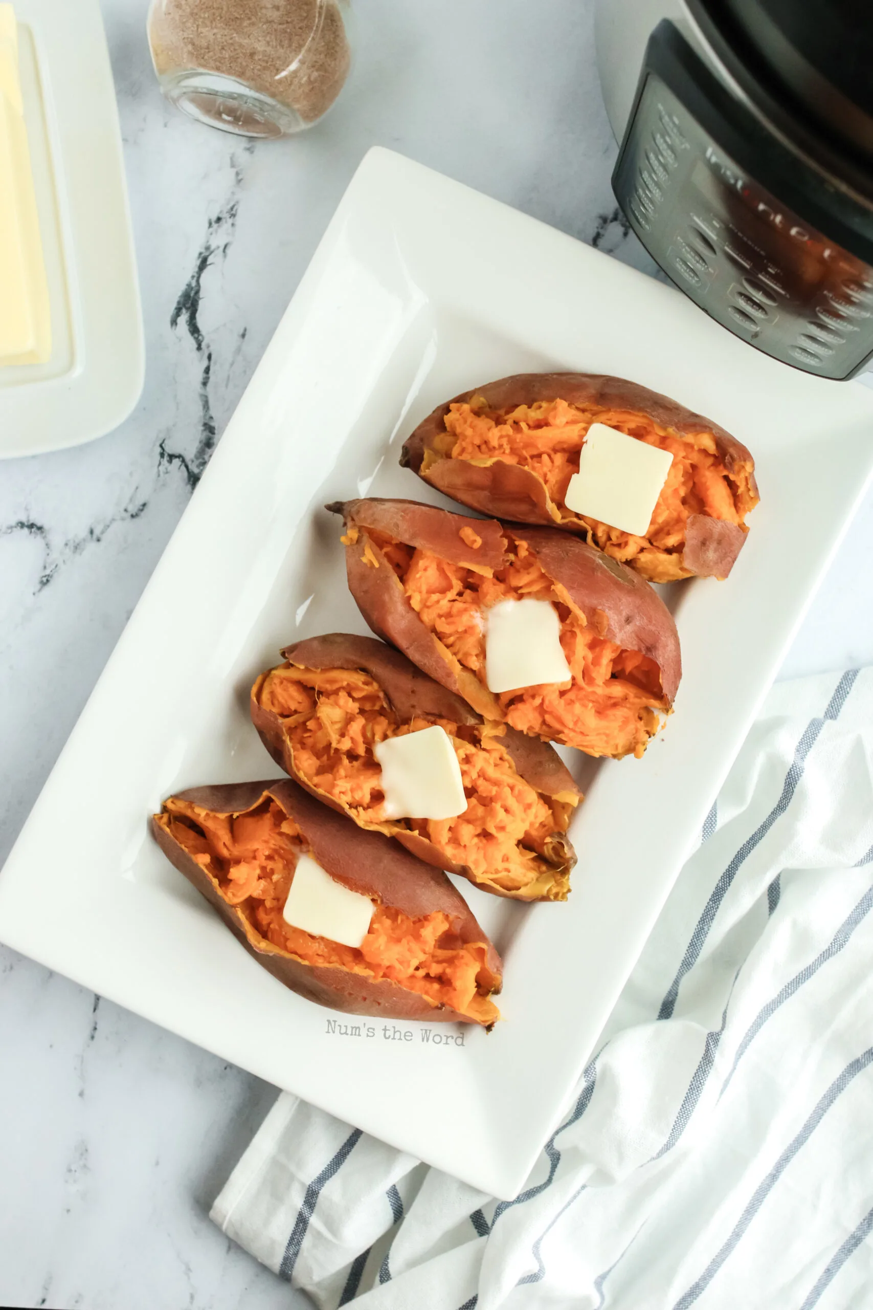 zoomed out image of 4 sweet potatoes on a platter with butter