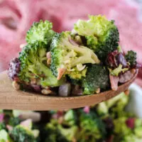 wooden spoon scooping a portion of broccoli salad out of the bowl