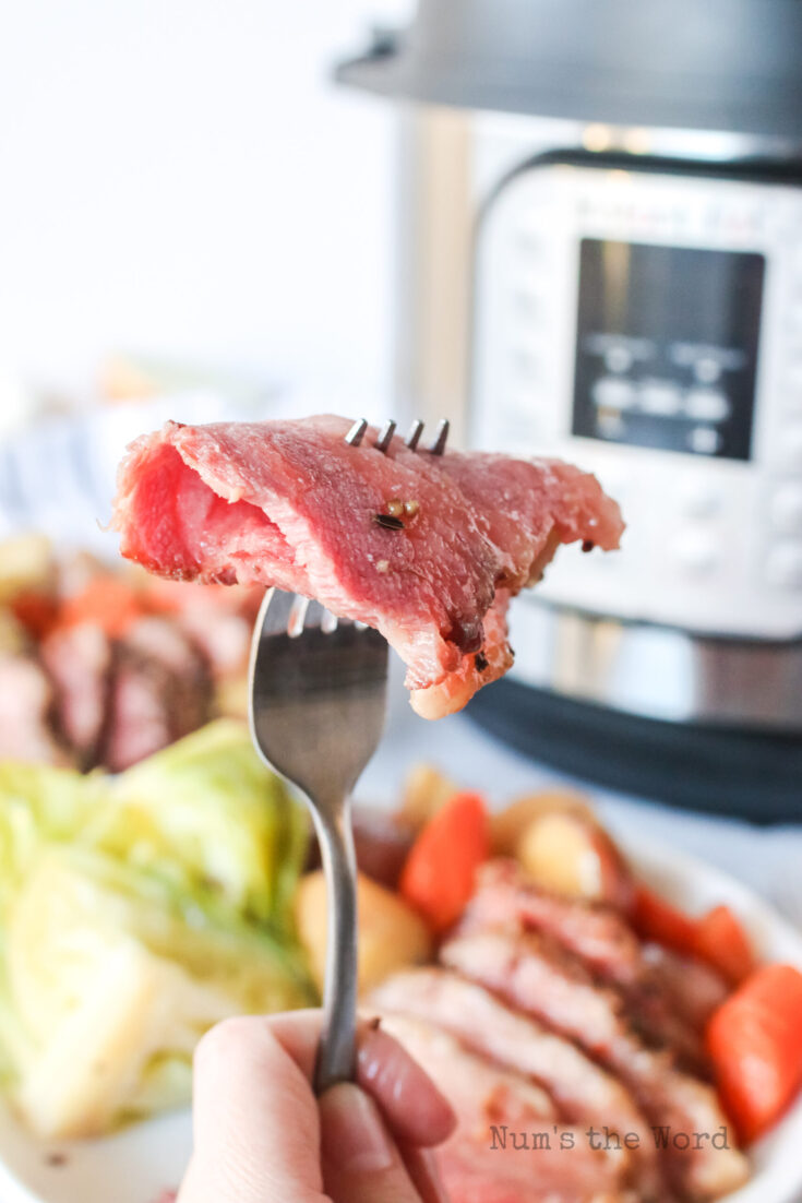 instant pot in background with a fork full of corned beef in the foreground.