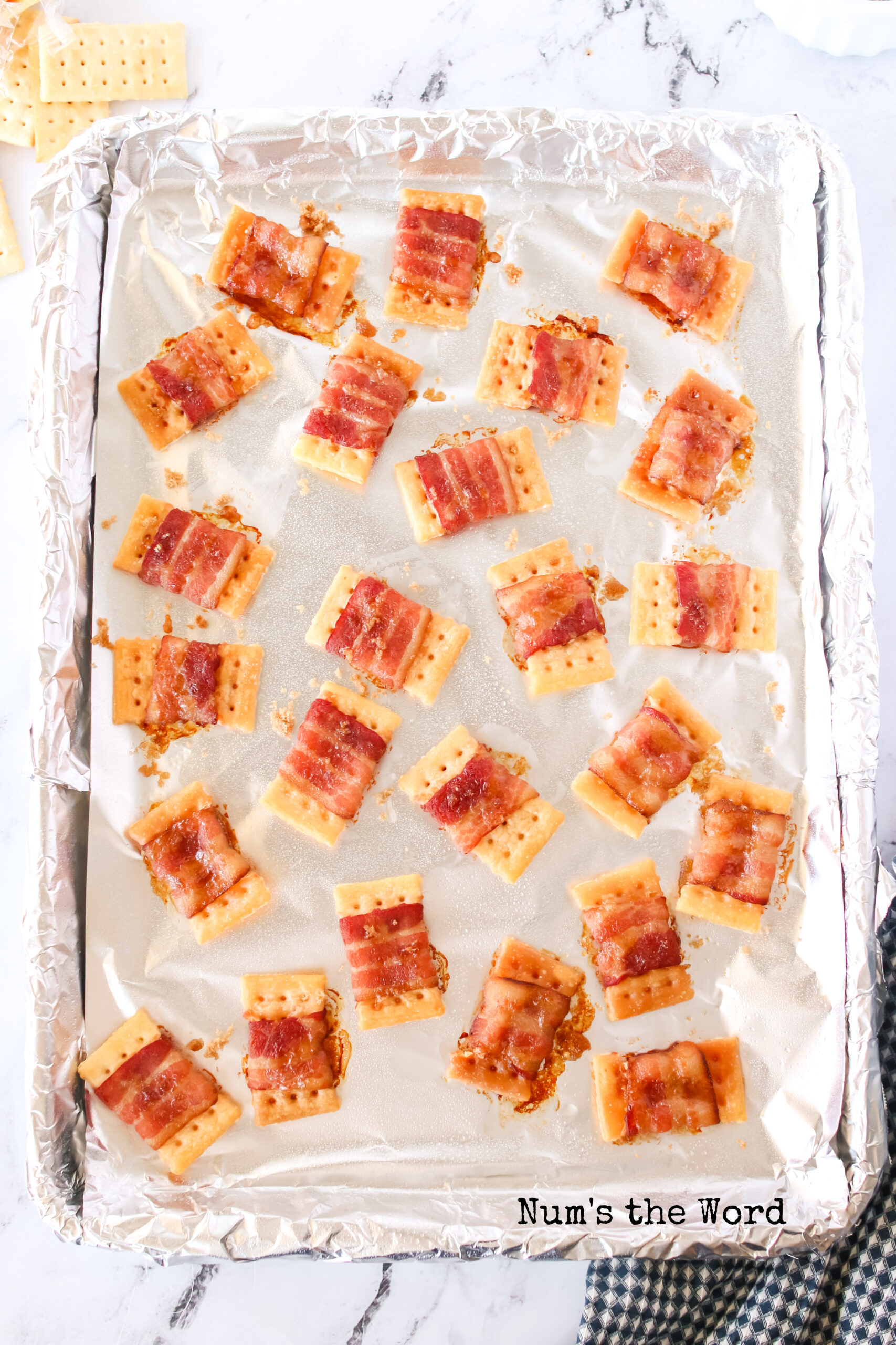crackers on cookie sheet, halfway cooked with a sprinkle of bacon on them.