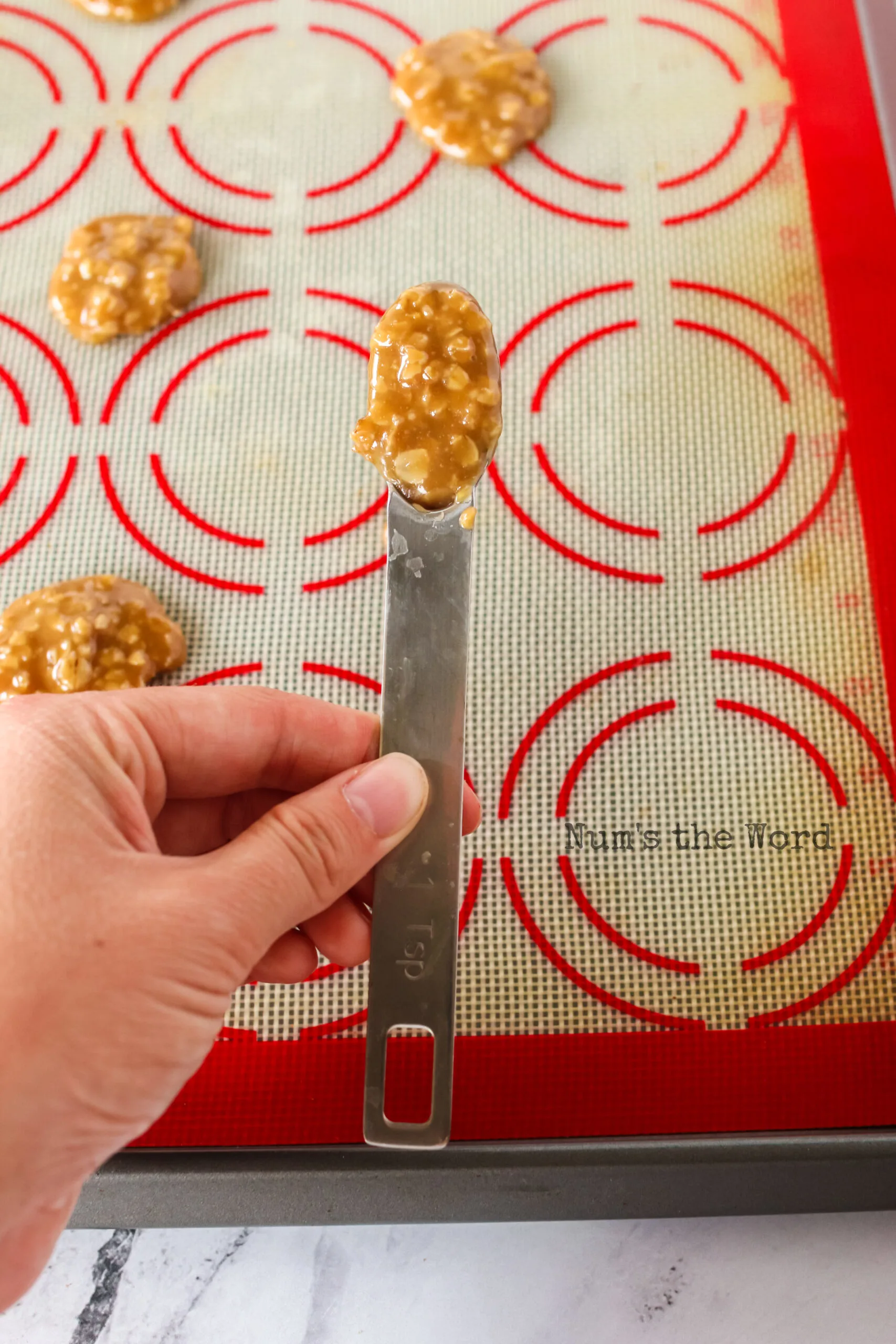 teaspoon of cookie mixture being placed on a silicone baking mat.