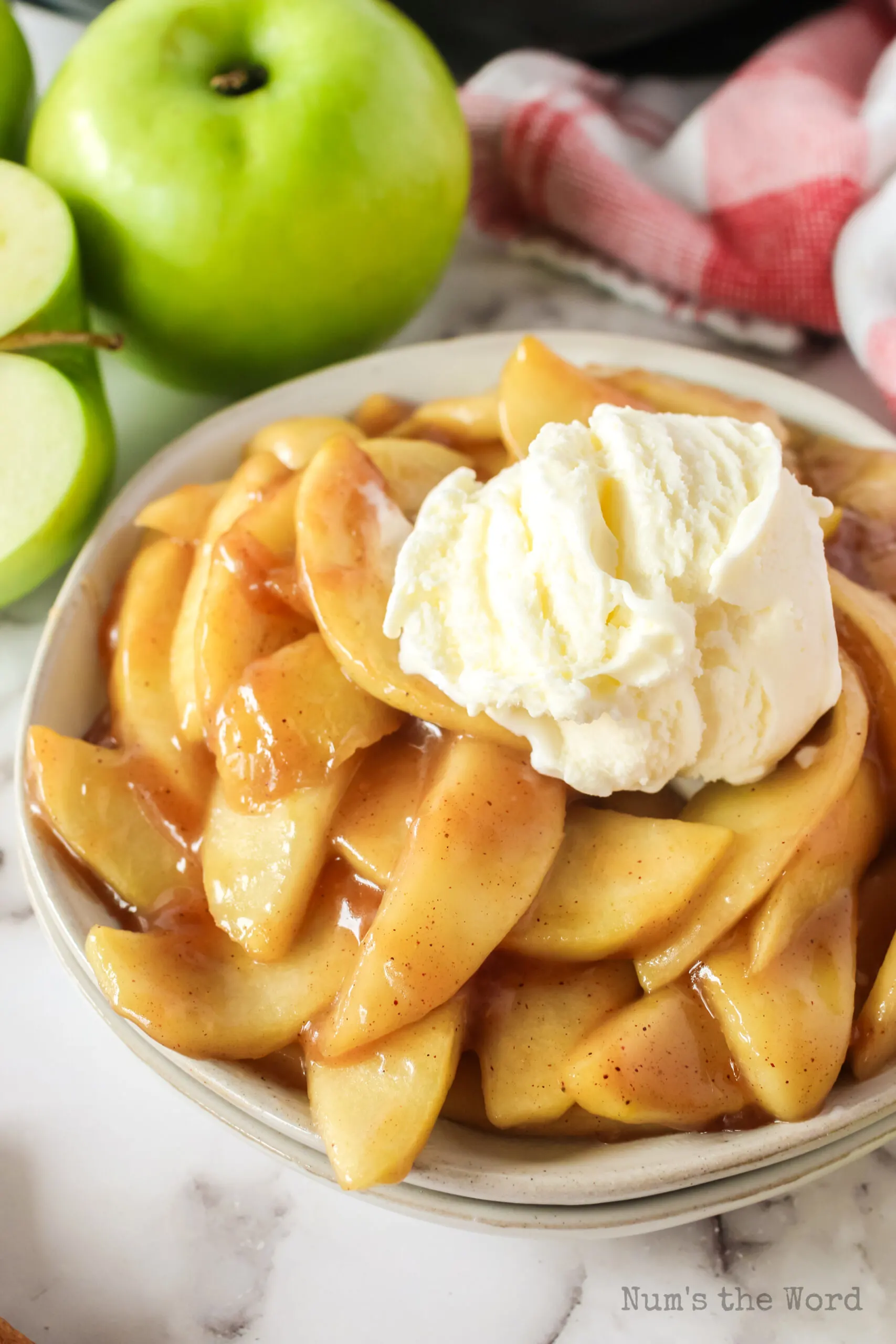 side view of apples on a plate with a scoop of vanilla ice cream.