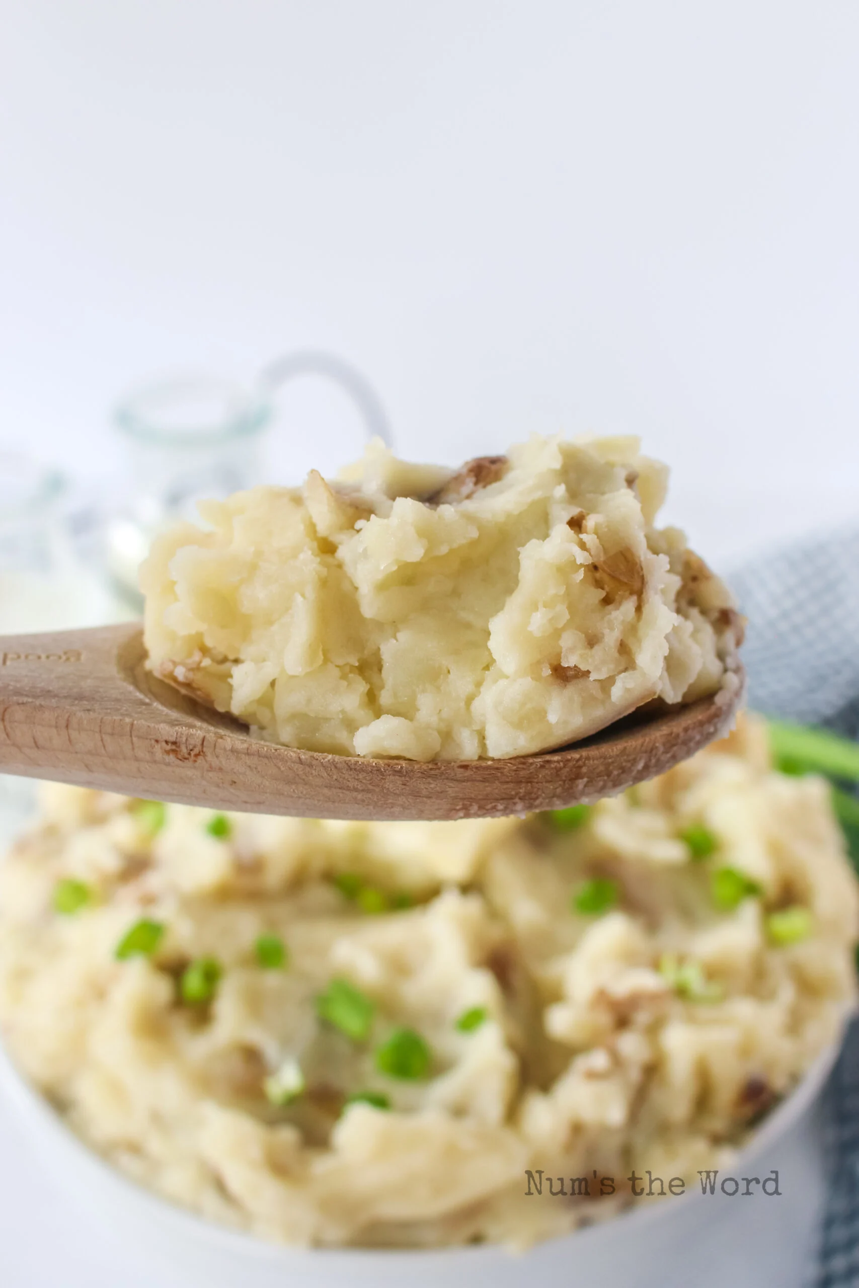 Side view of mashed potatoes in a serving bowl with a wooden spoon scooping a portion out.