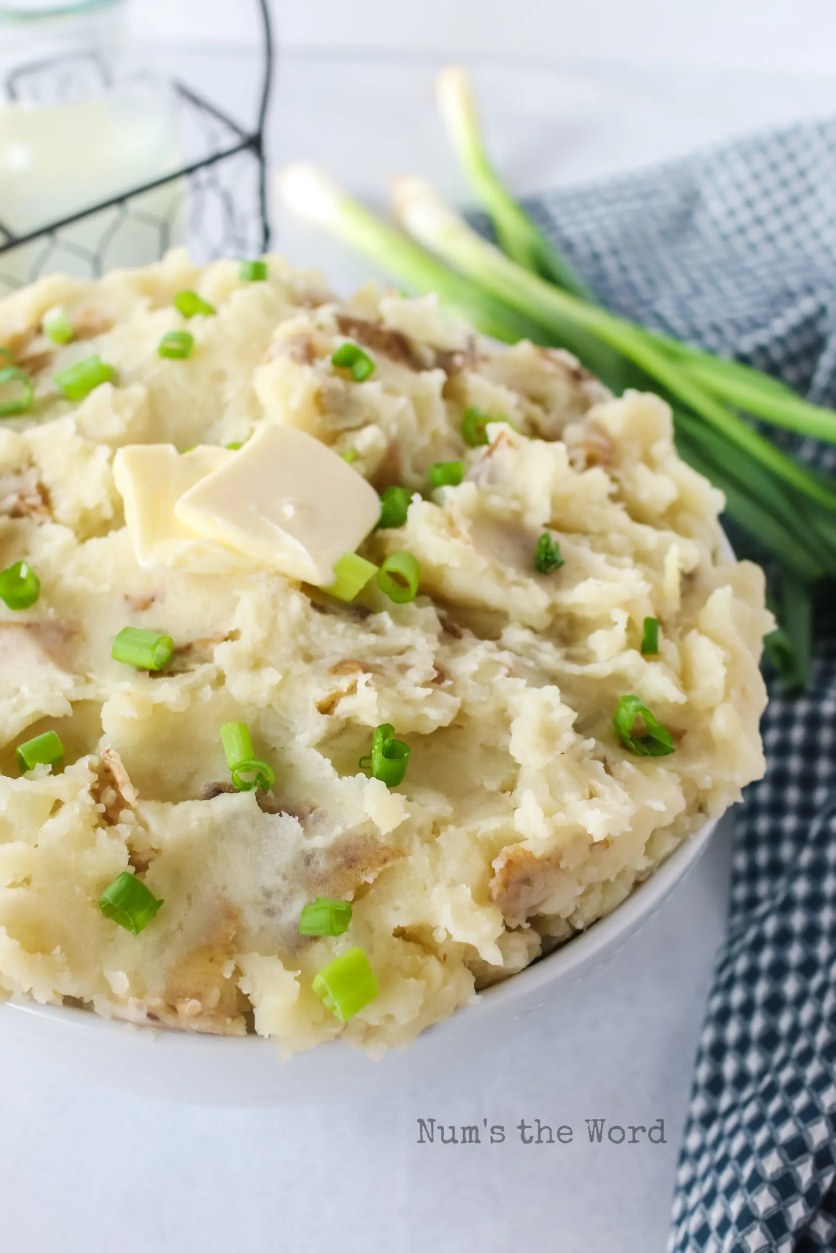 side view of mashed potatoes in a bowl with butter and green onions.