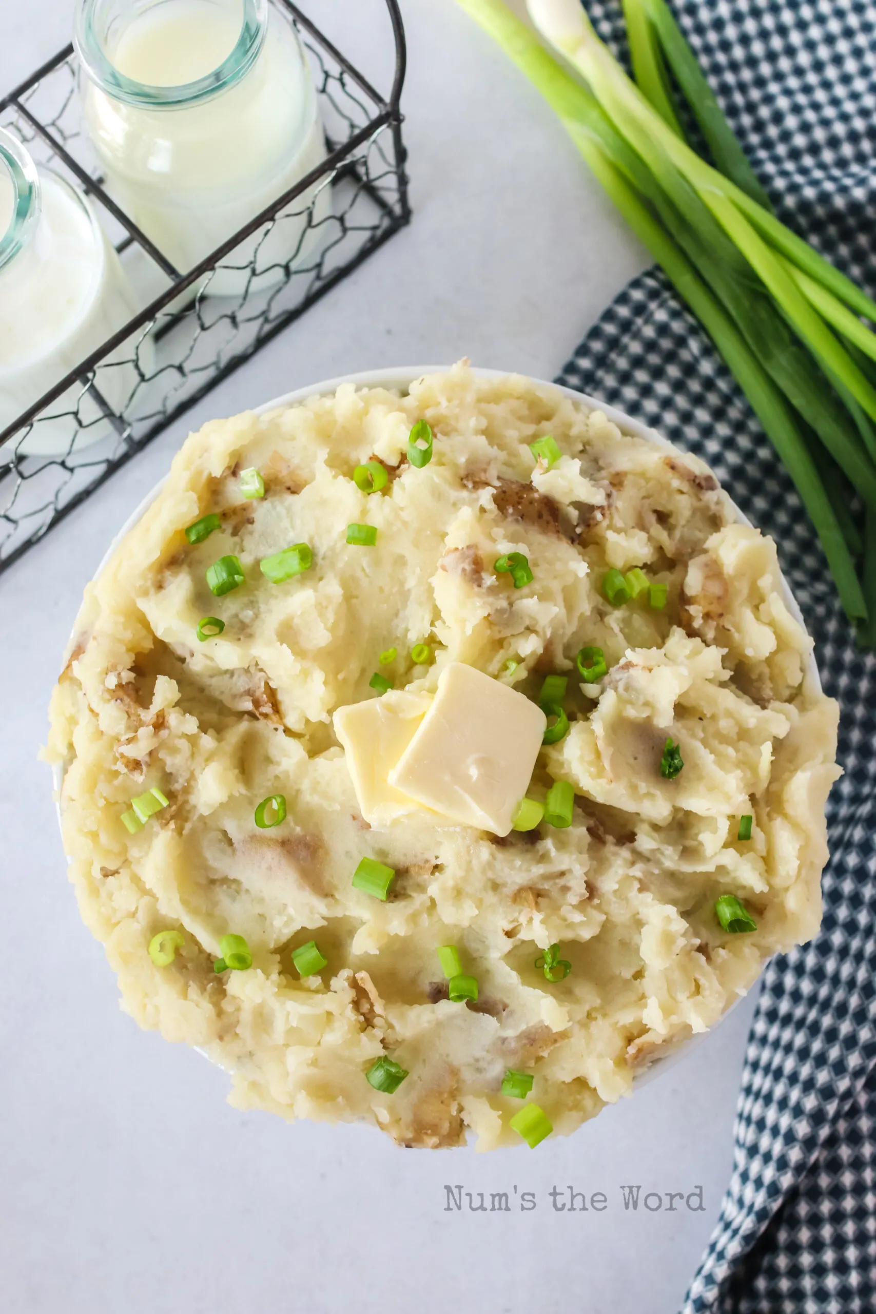 zoomed out image of mashed potatoes in a bowl topped with butter and green onions.