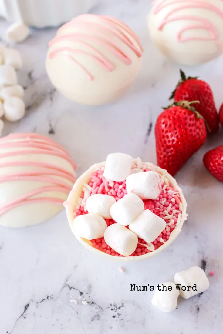 2 full hot cocoa bombs in the background. 1 hot cocoa bomb opened and showing filling