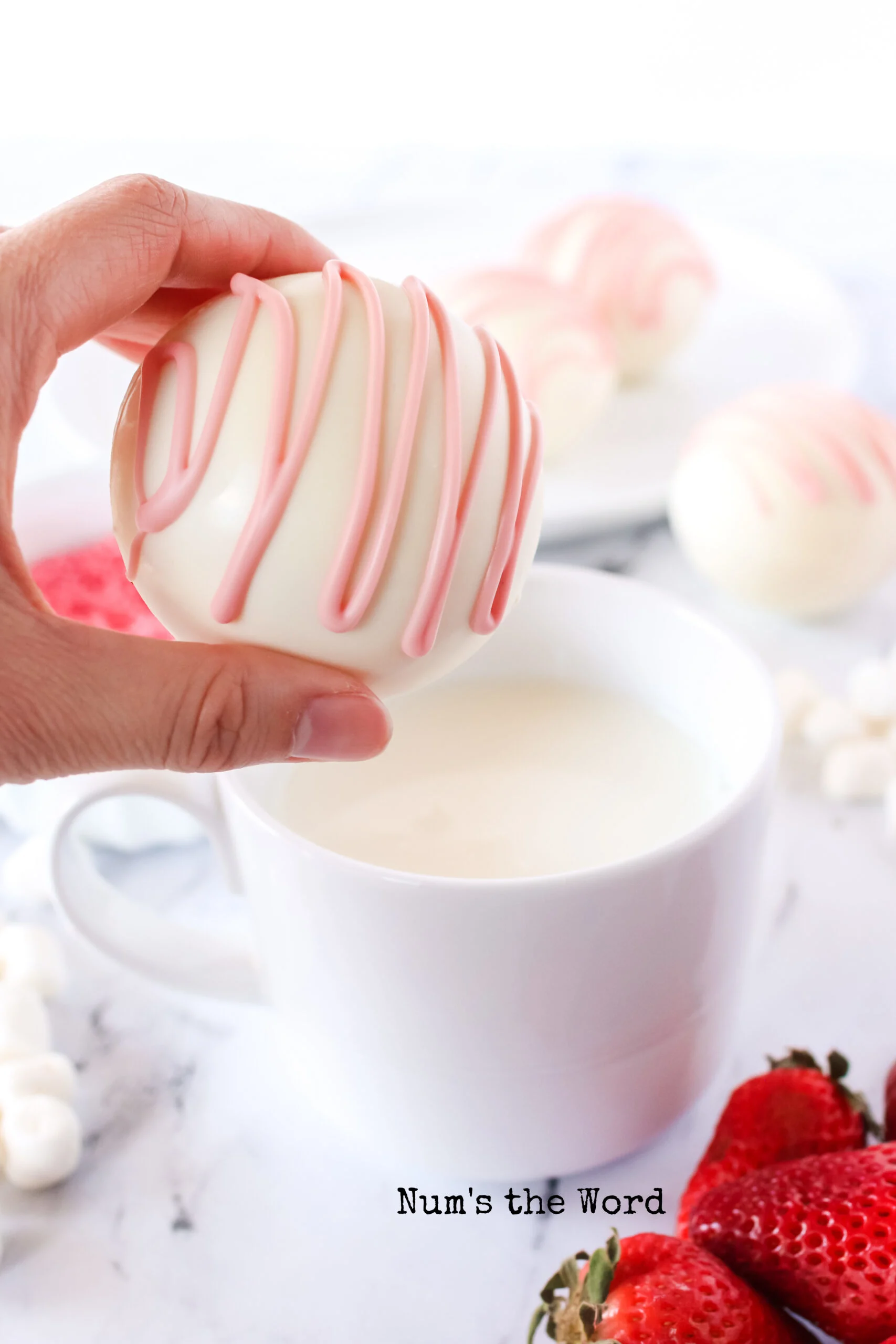 hand holding a single hot cocoa bomb about to drop it in a cup of hot milk.