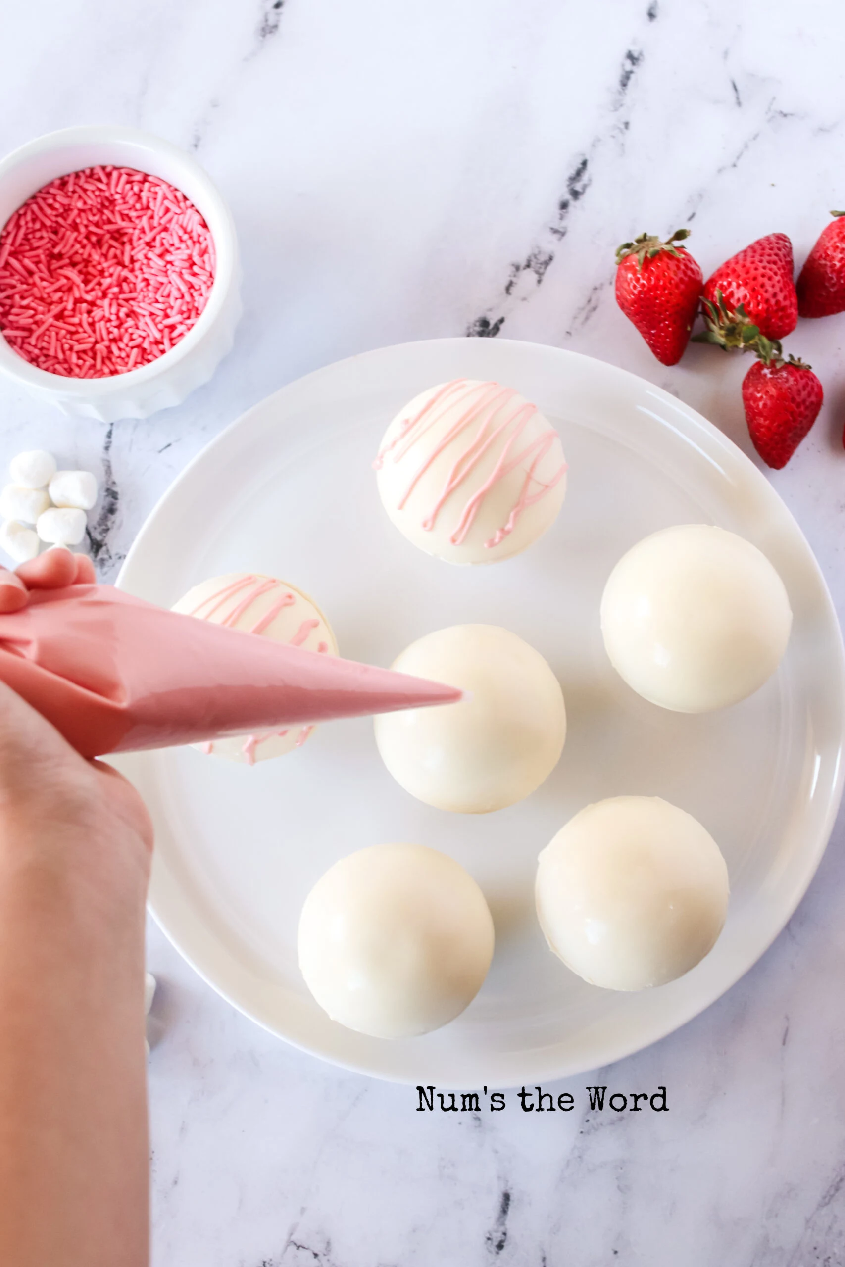 Pink chocolate being drizzled on top of hot cocoa bombs