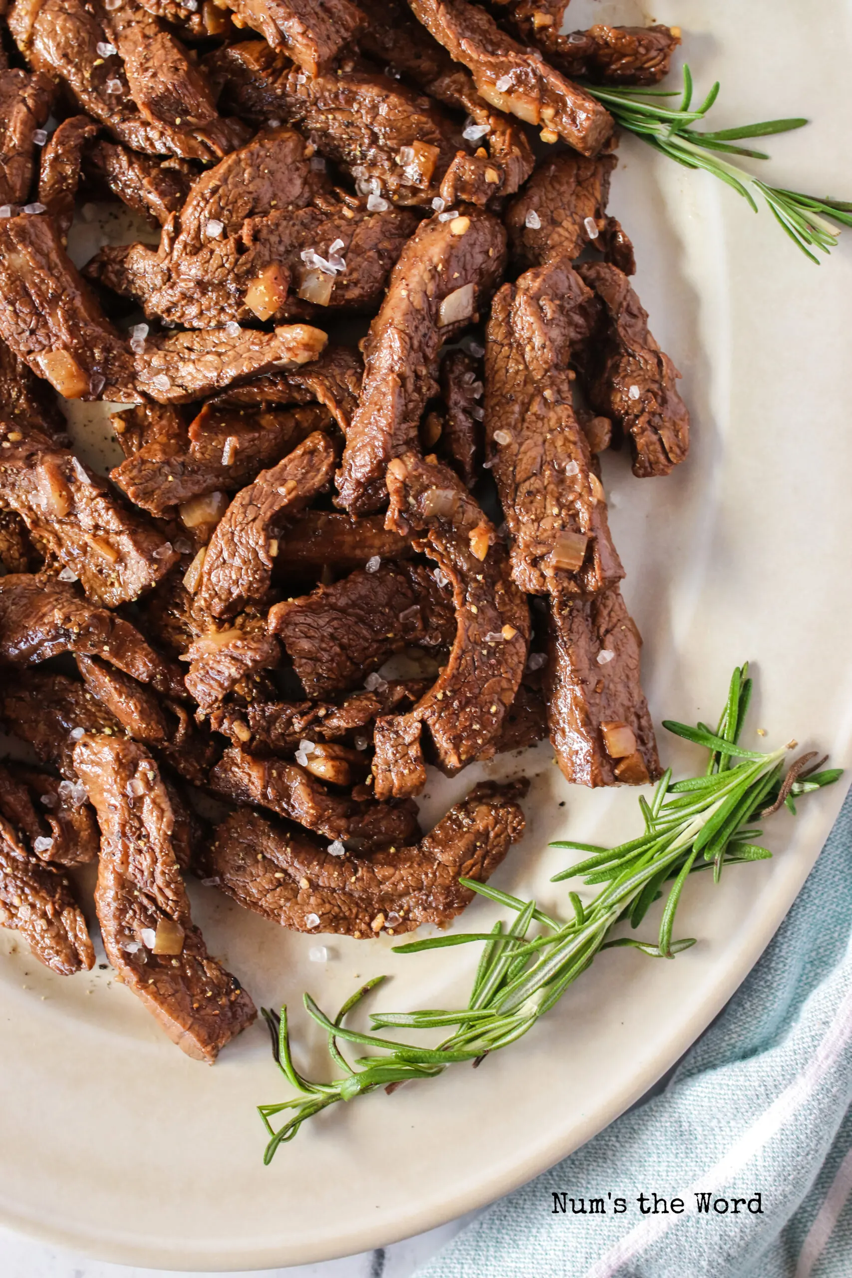 cooked balsamic flank steak on a platter with black pepper and coarse sea salt