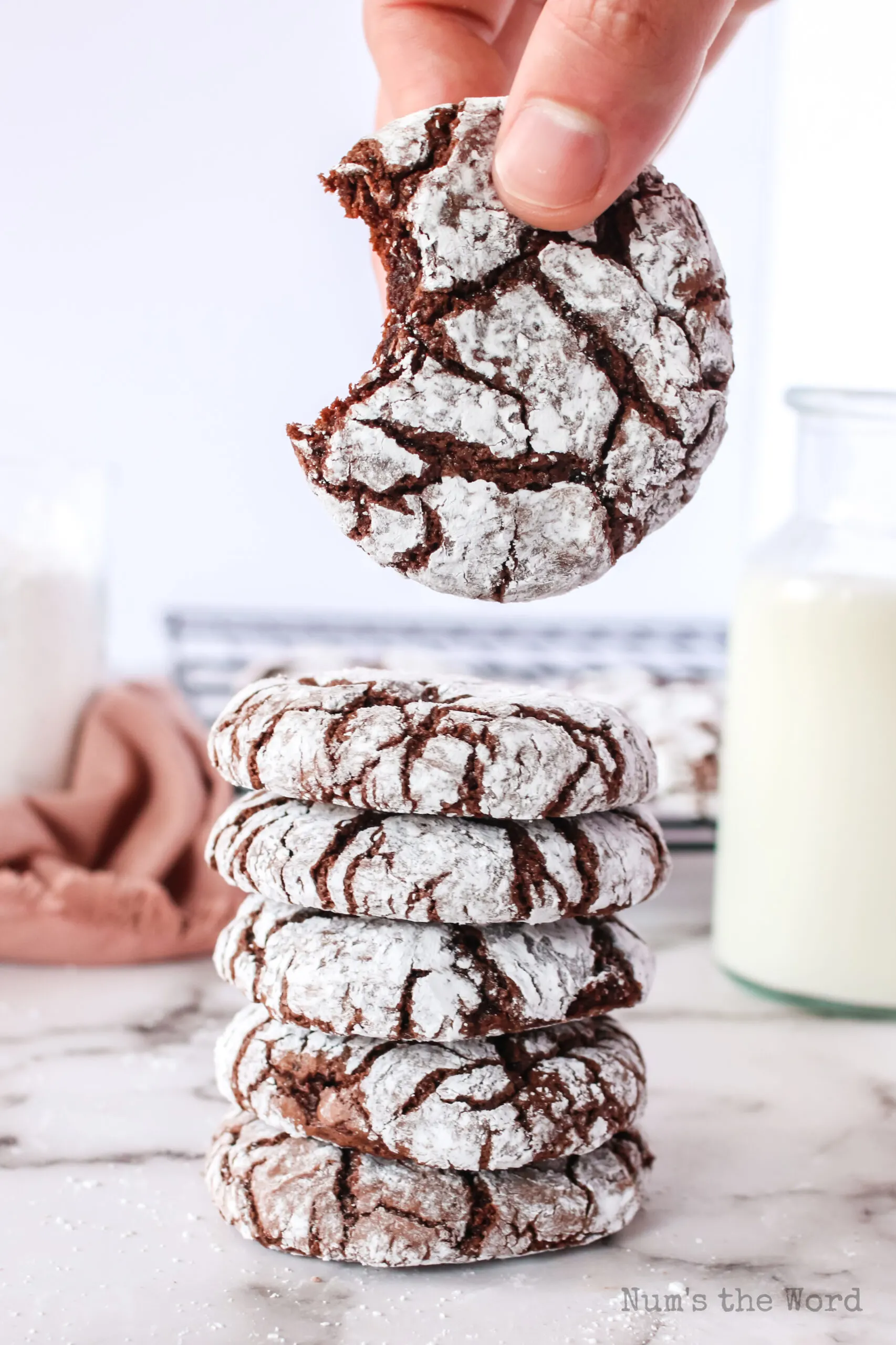 5 cookies stacked up with a cooking being held above the stack. Cooking being held has a bite removed.