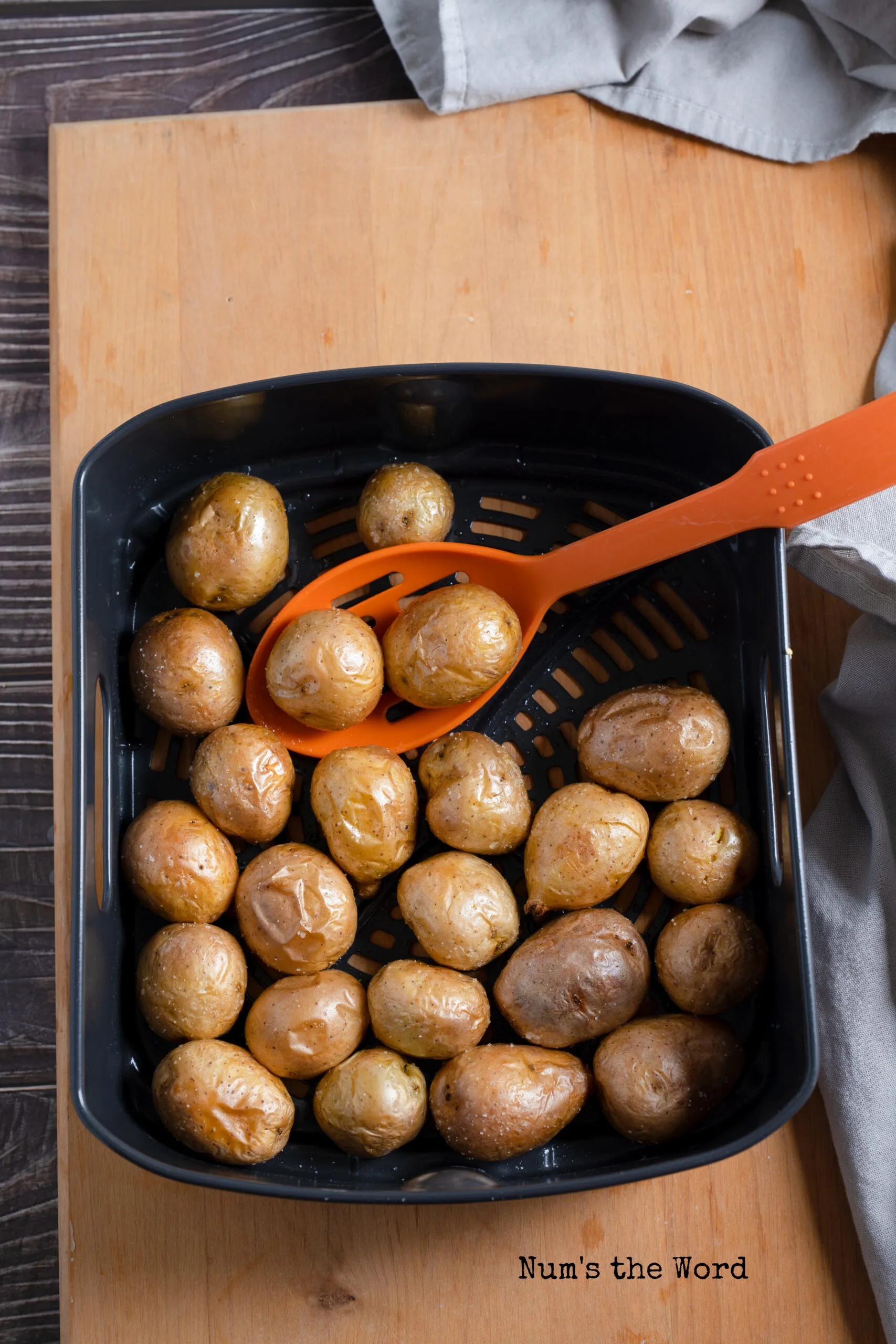 cooked baby potatoes being scooped out of air fryer with a slotted spoon
