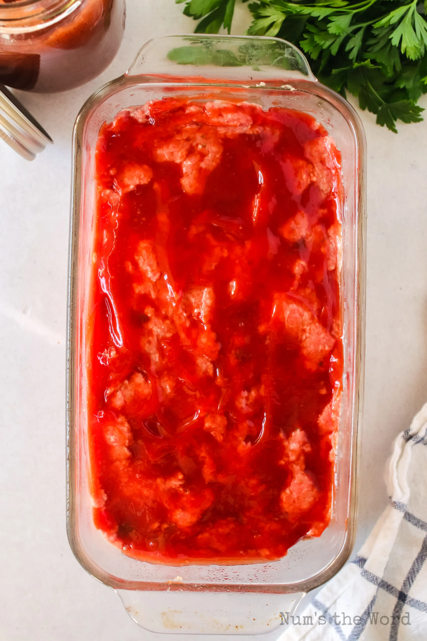 red sauce spread over the top of meatloaf in bread pan.