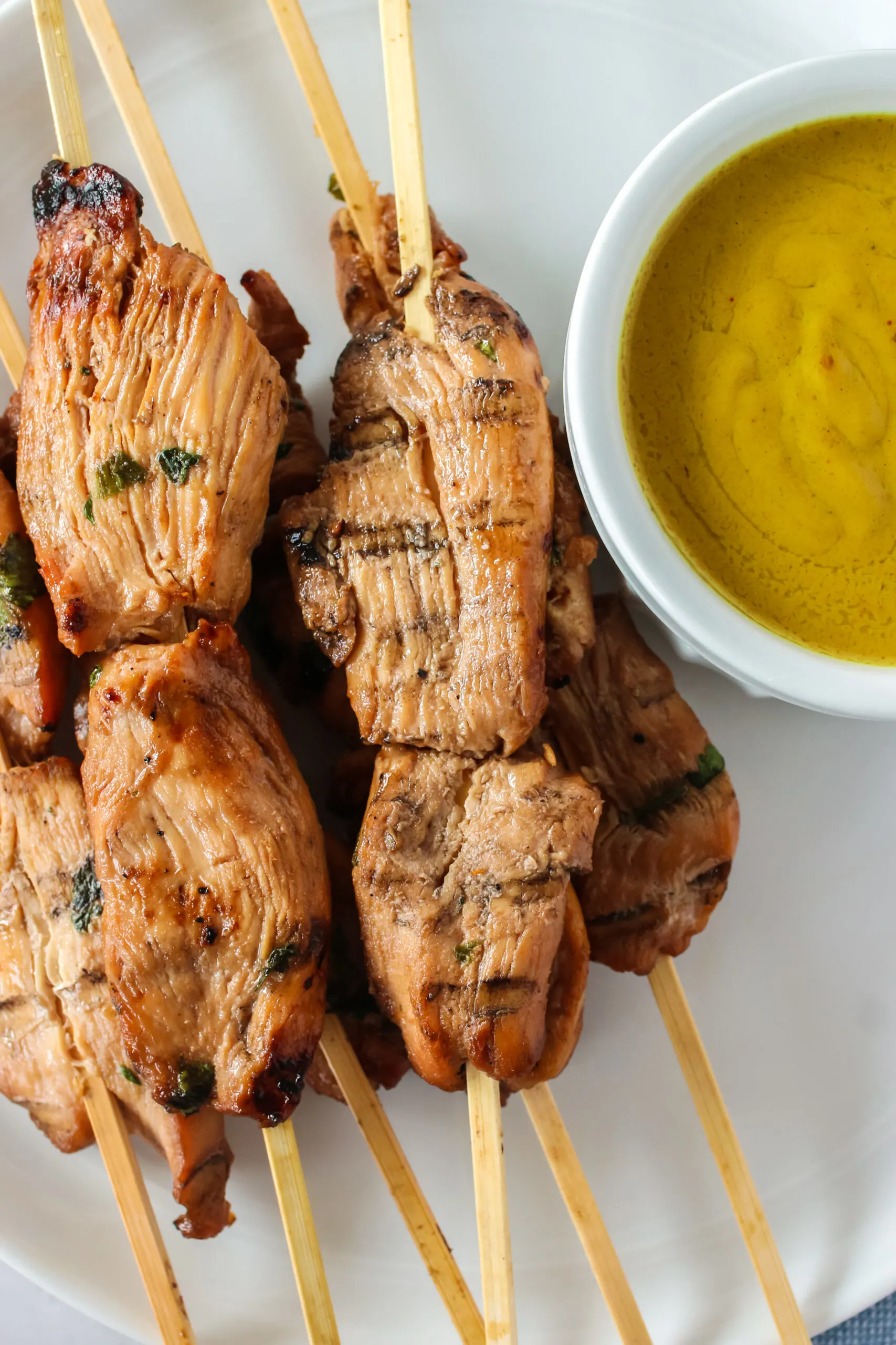 photo looking down on cooked chicken skewers on a plate with peanut sauce.