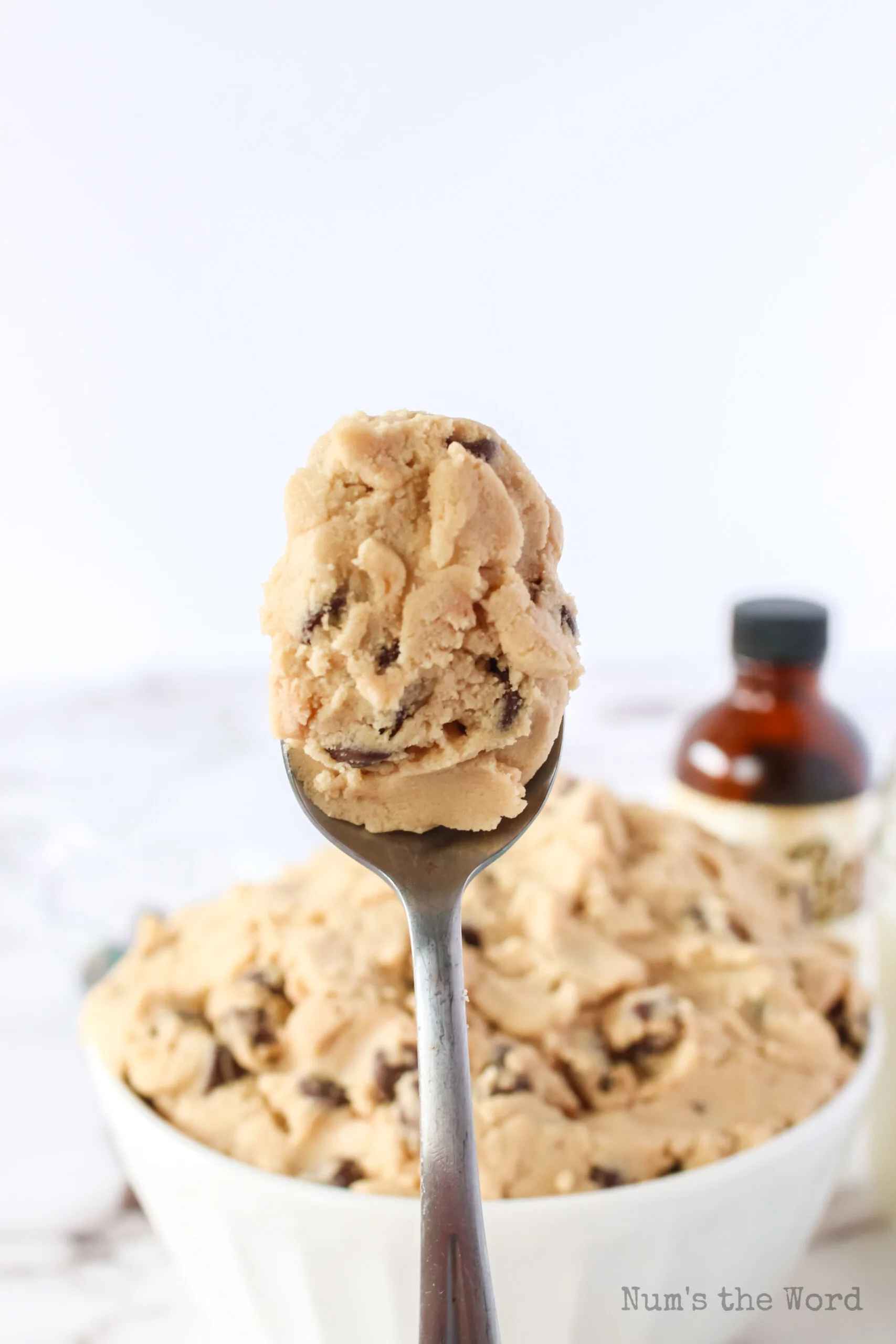 spoonful of cookie dough being held in air with bowl in background.
