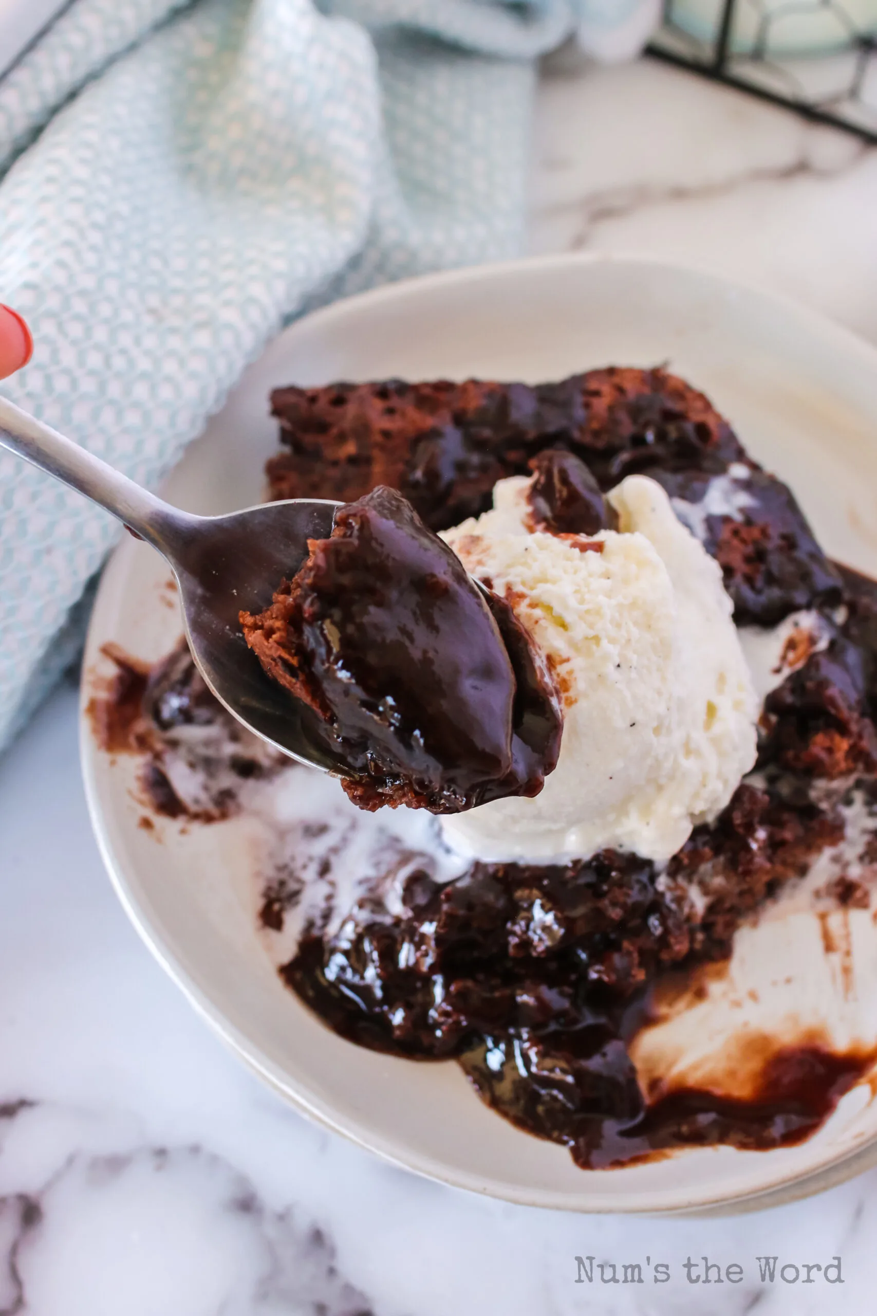 spoon being held up with a scoop of chocolate cobber, being held above plate full.