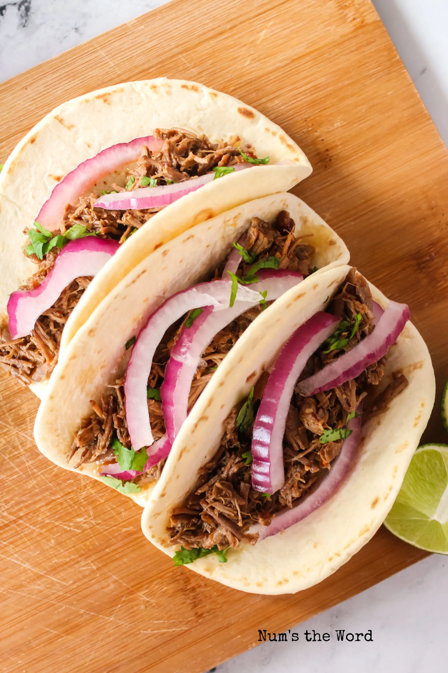 close up of 3 tacos on a serving board.