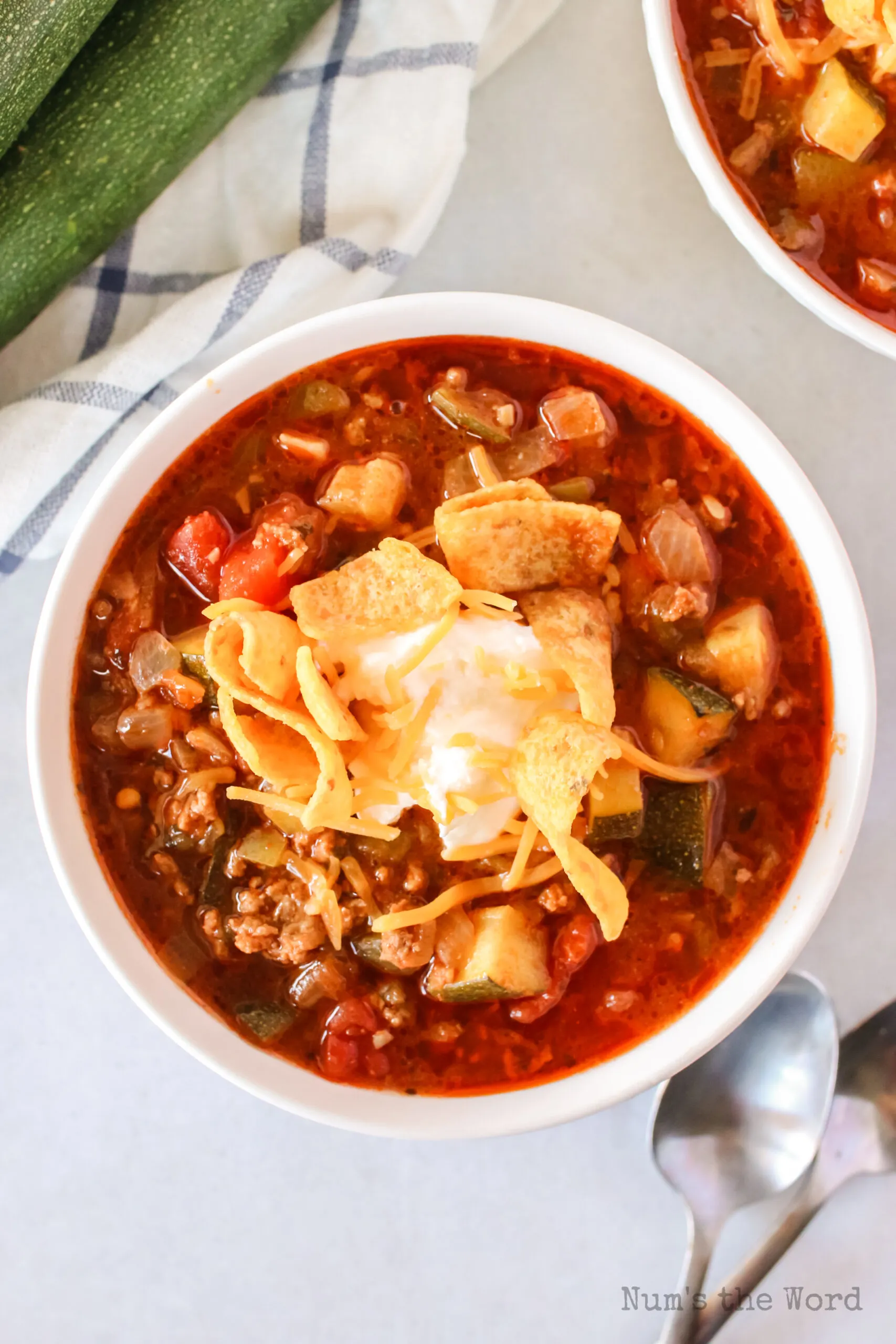 bowl of zucchini chili in a bowl with cheese, sour cream and Fritos on top.